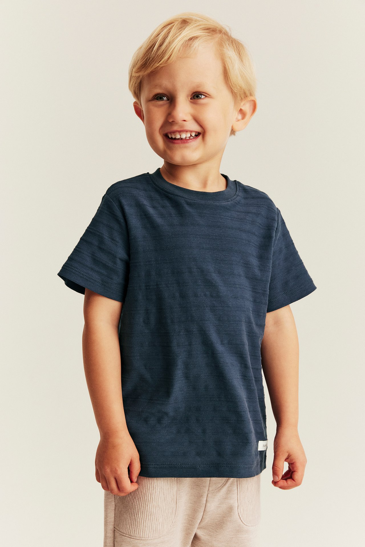 Front view of a kid in a dark blue textured t-shirt and light beige ribbed shorts.