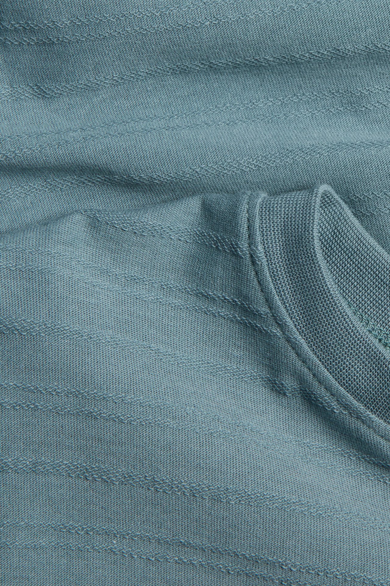 Close-up of a blue-green ribbed fabric garment with a folded ribbed knit neckline.