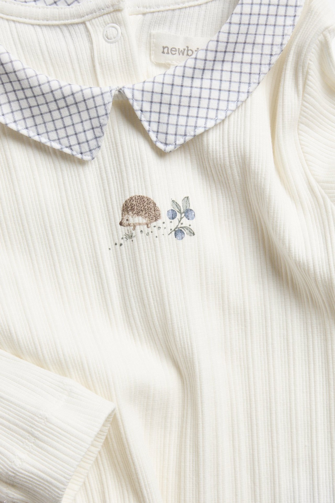 Nahaufnahme Vorderansicht eines cremefarbenen gerippten Langarm-Babybodys mit kariertem Kragen und Igel-Print.