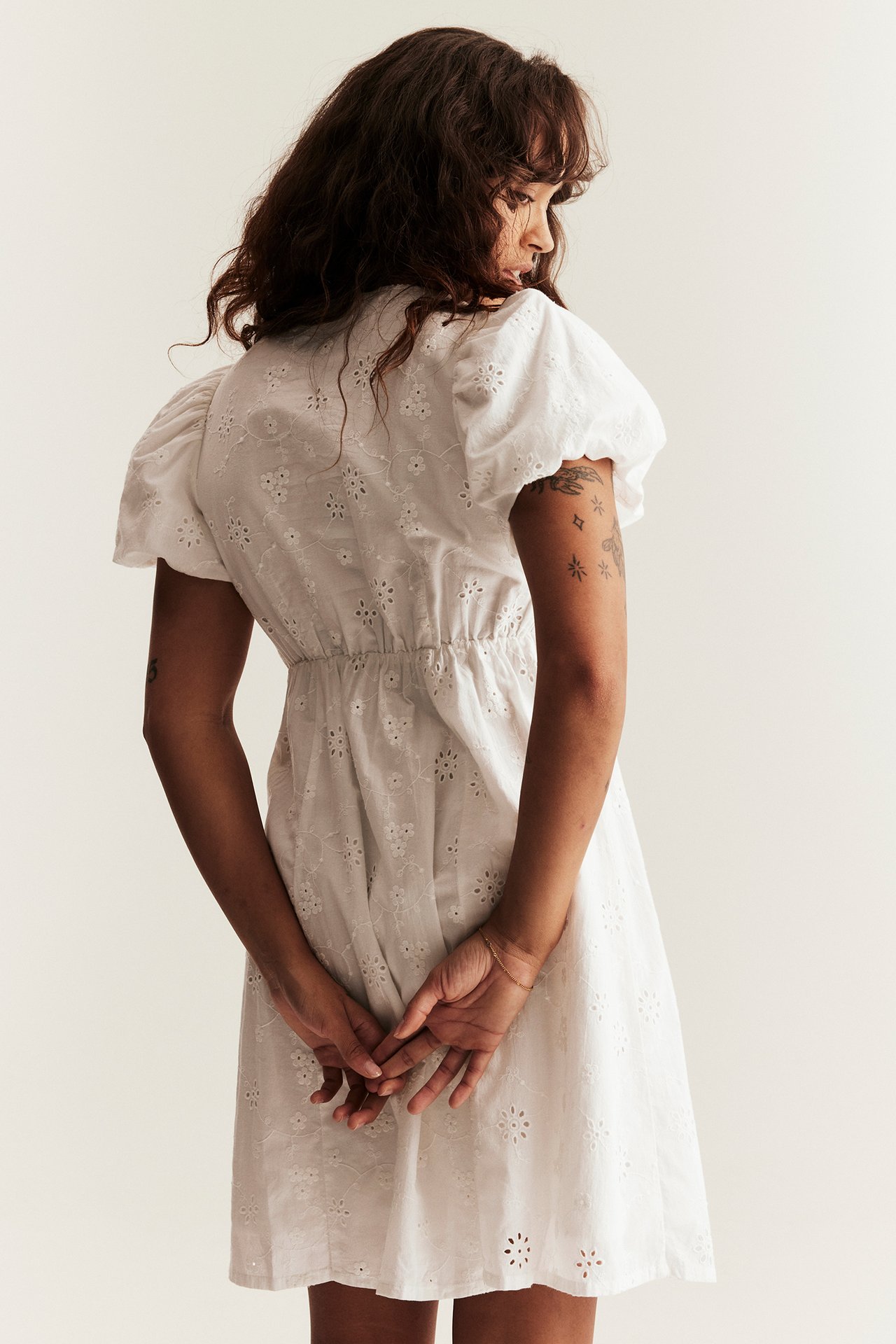 Back view of a woman in an off-white embroidered cotton dress with short puffy sleeves and an elasticated waist.