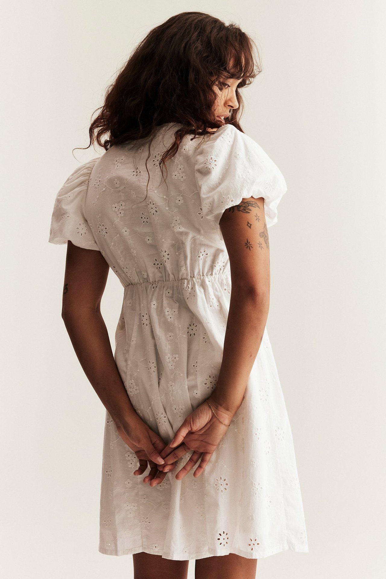 Back view of a woman in an off-white embroidered cotton dress with short puffy sleeves and an elasticated waist.