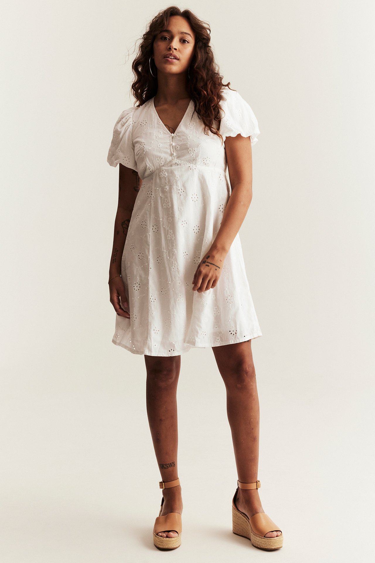 Front view: Woman in off-white embroidered cotton dress with puff sleeves and tan espadrille wedges.