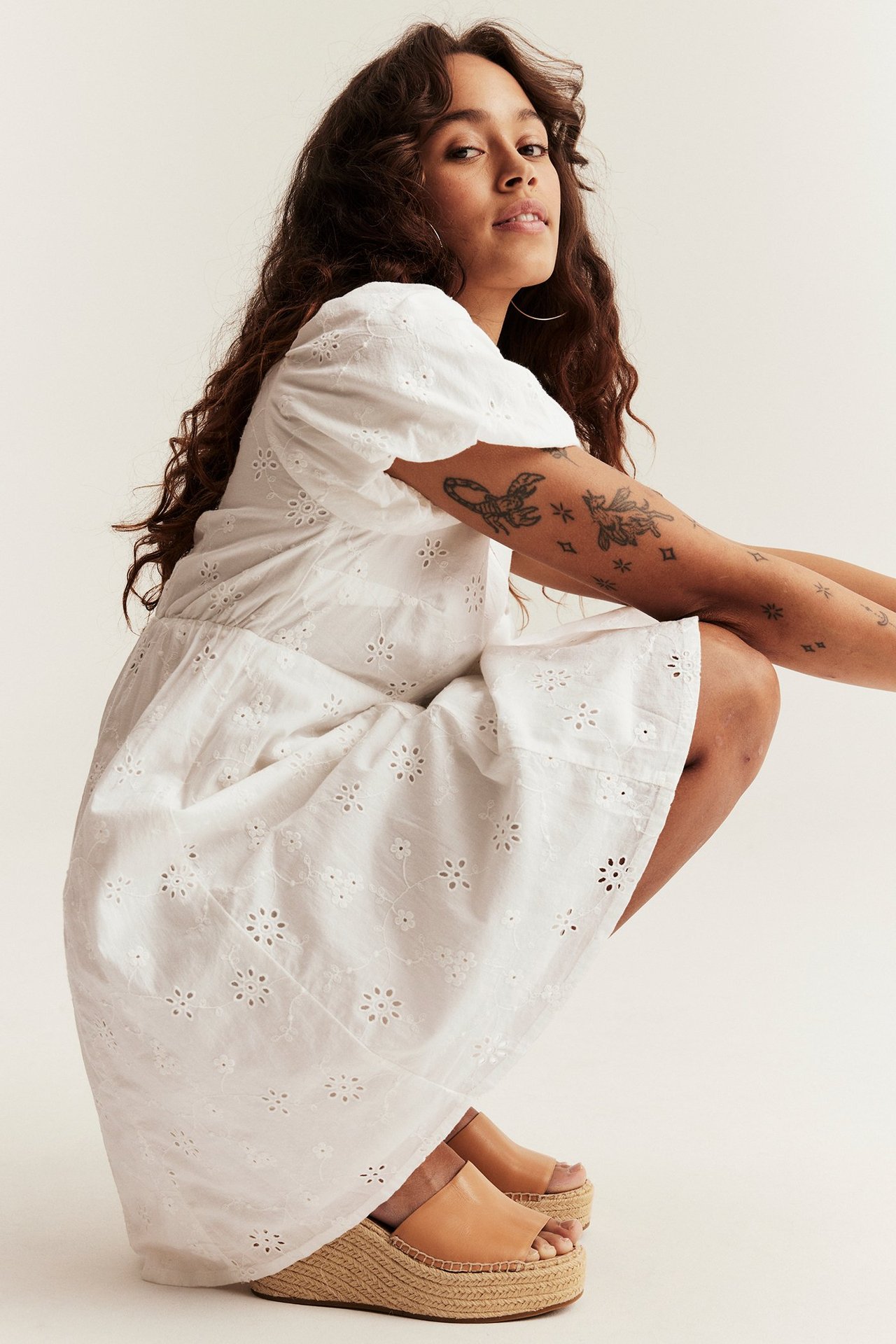 Side view of a woman wearing an offwhite embroidered cotton dress with puff sleeves and tan espadrille platform sandals.