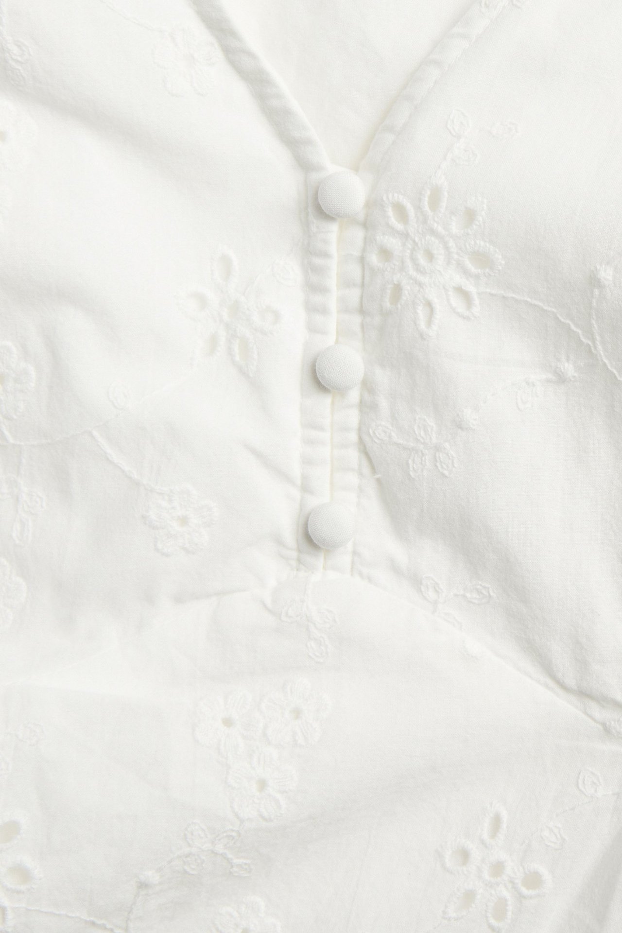 Close-up of an off-white cotton dress with tone-on-tone floral embroidery and covered buttons.