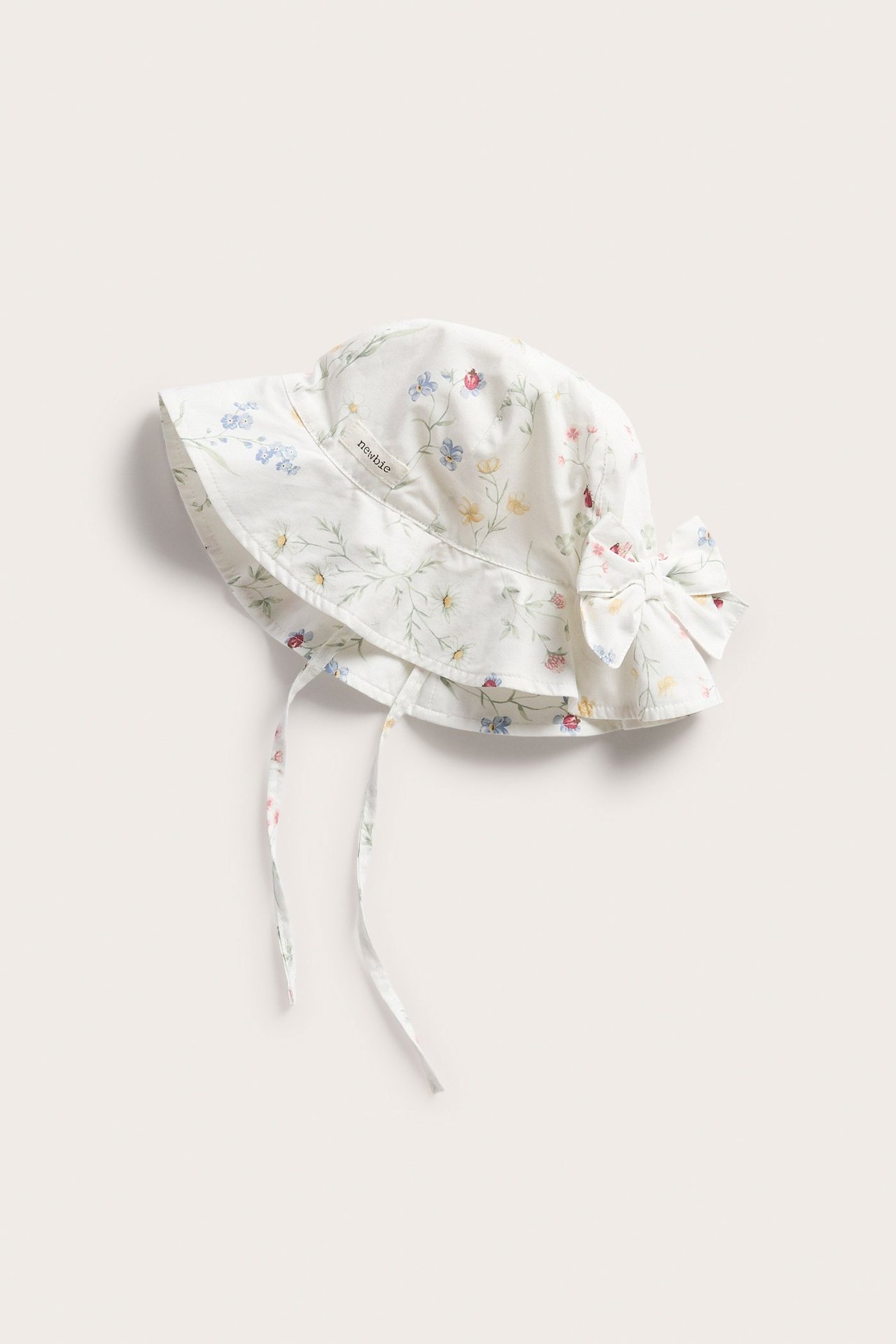 Frontalansicht eines off-white geblümten Baby-Sonnenhuts mit Schleife hinten und Bindebändern.
