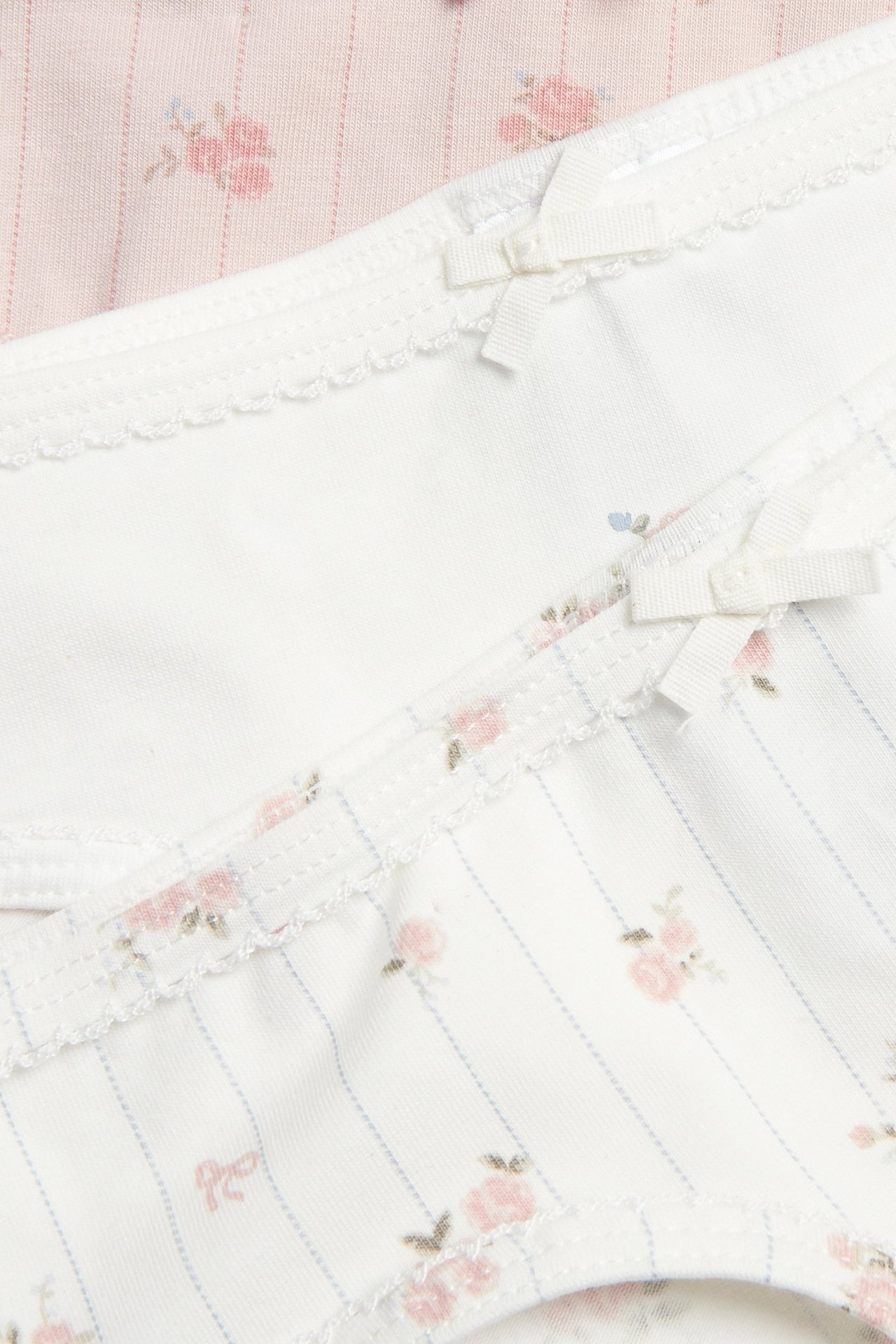 Nahaufnahme: drei geblümte Baumwollslips, cremeweiß gestreift, cremeweiß, rosa, mit Schleifen und Zierkanten.