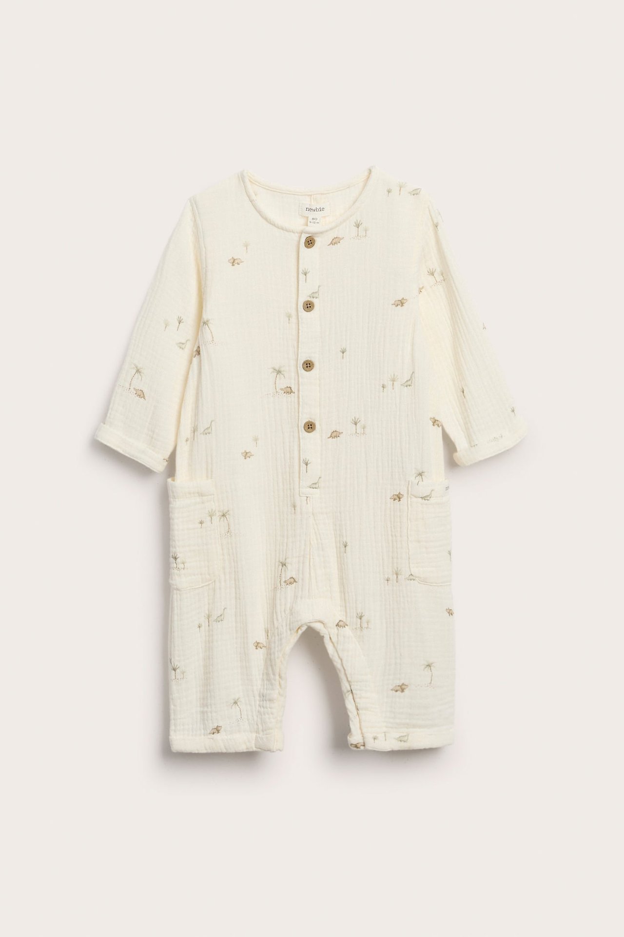 Vorderansicht: Offwhite Baby-Musselin-Overall mit Palmen- und Dinosaurier-Print, Frontknöpfen, hochgekrempelten Ärmeln.