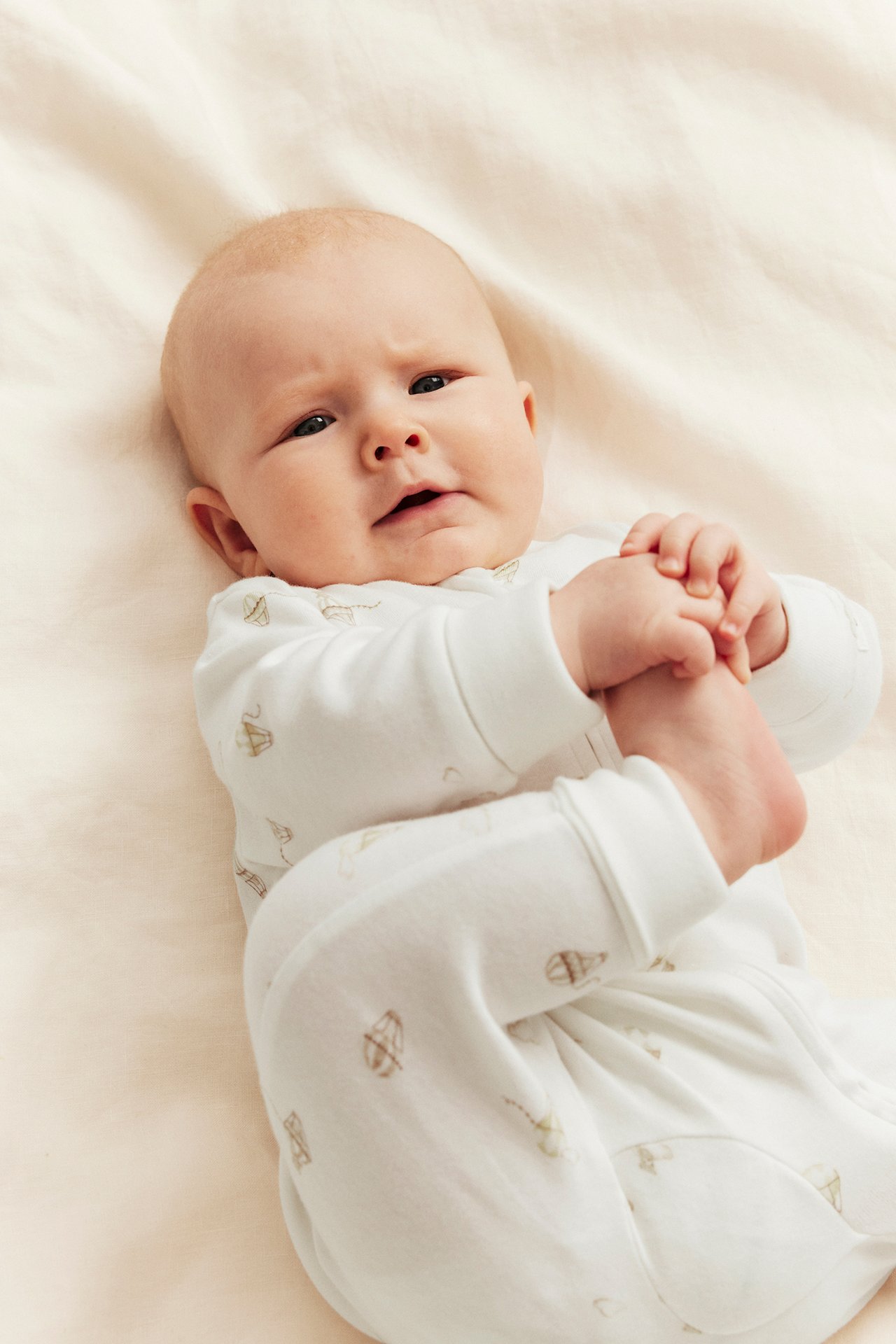 Vorderansicht: Baby in cremeweißem Baumwoll-Romper mit Heißluftballonmuster und Reißverschluss vorne.