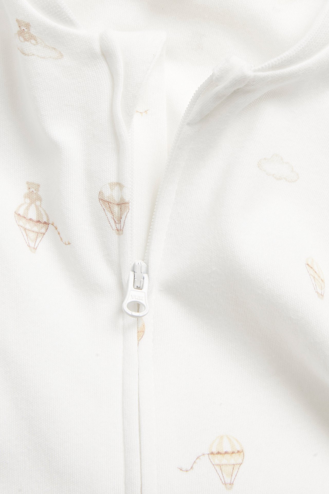 Close-up of an off-white baby romper with light brown hot air balloon pattern and a front zipper.