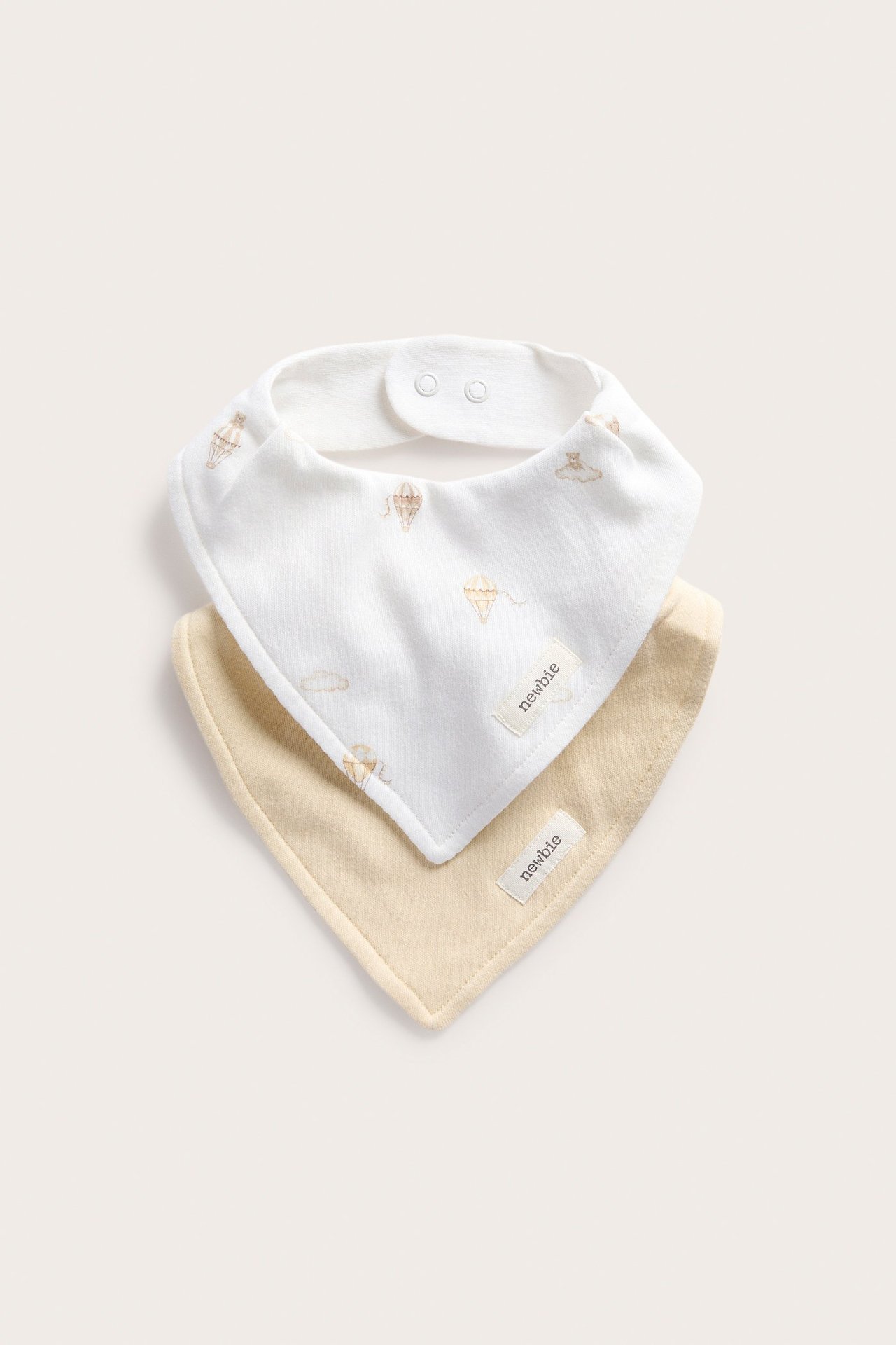 Vorderansicht: Zwei Baby-Halstücher. Eines cremeweiß mit Heißluftballons, eines hellgelb, beide mit Druckknöpfen.