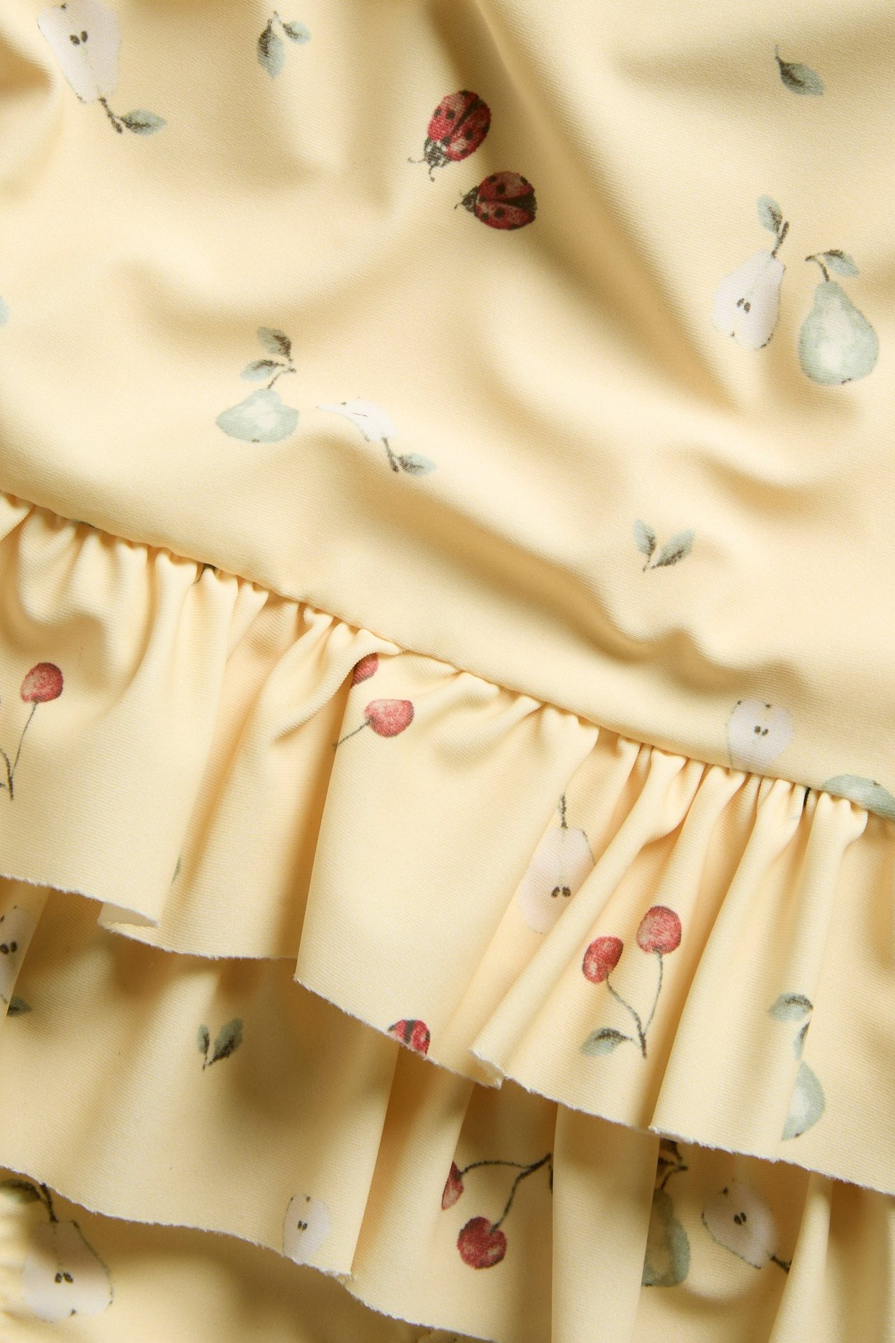 Close-up: yellow patterned swimsuit with fruit print and ruffle details.