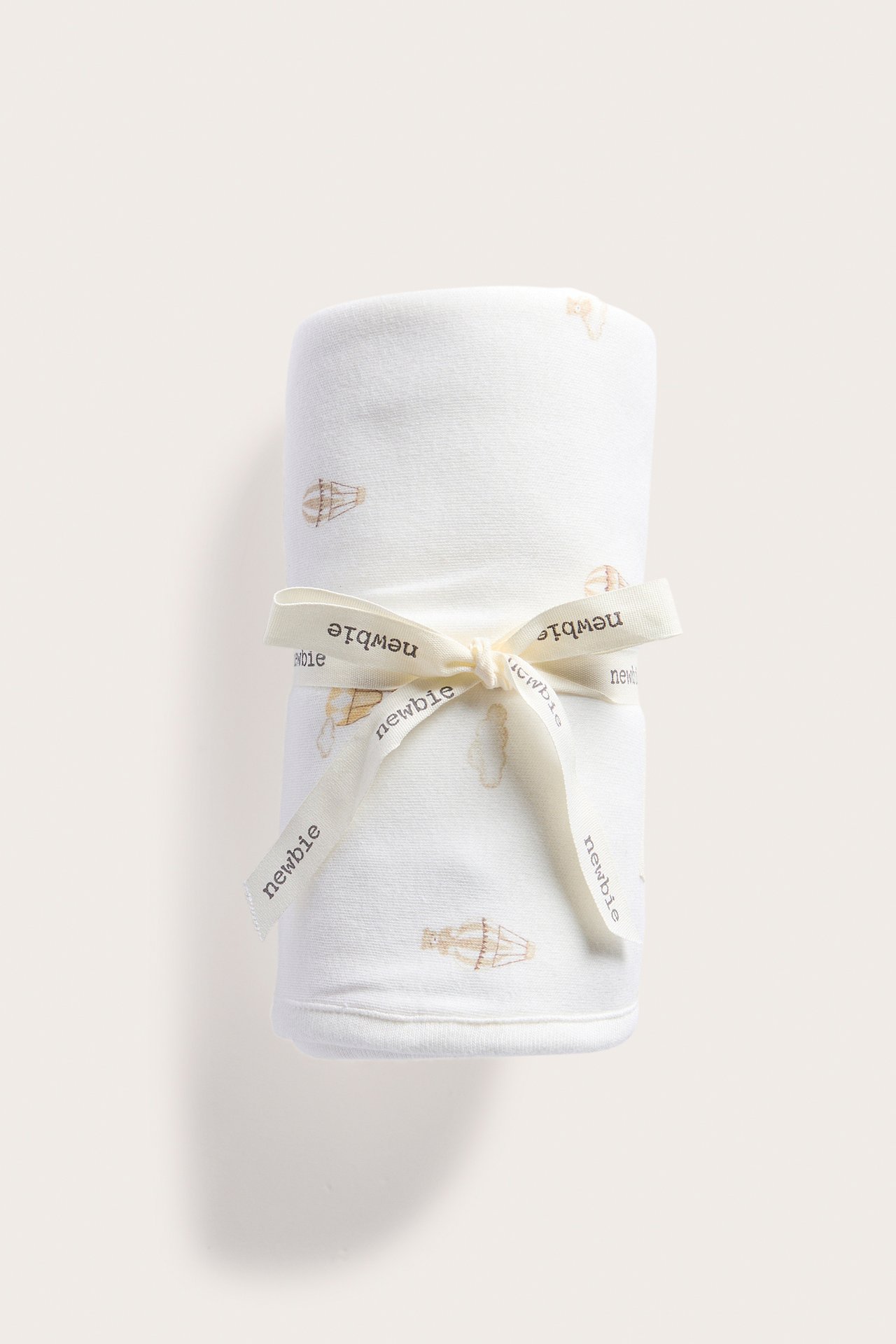 Vorderansicht einer cremeweißen Baumwoll-Babydecke mit Heißluftballonmuster, mit einem cremefarbenen Band gebunden.