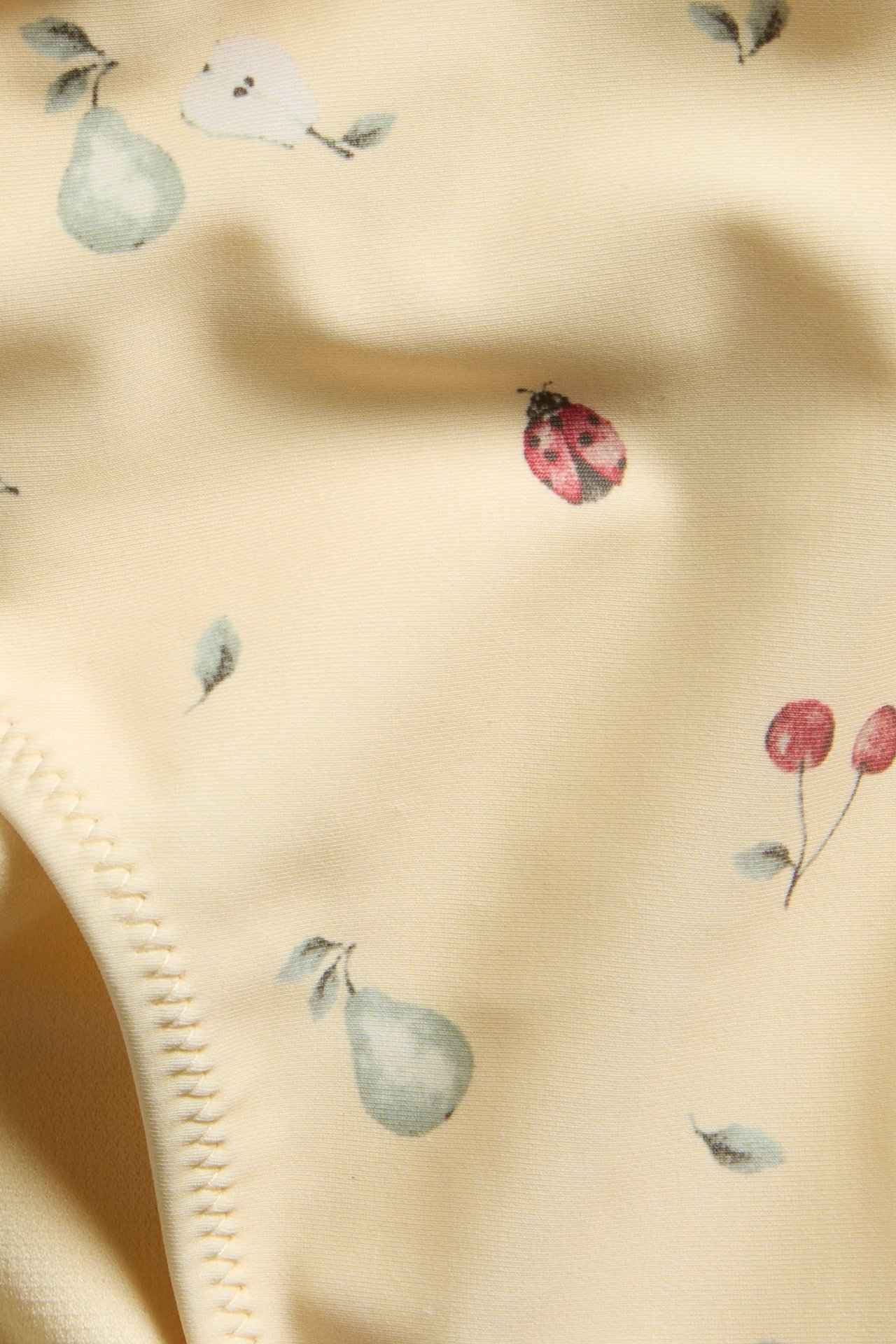 Close-up of yellow patterned bikini bottoms with green pears, red ladybugs, and cherries.