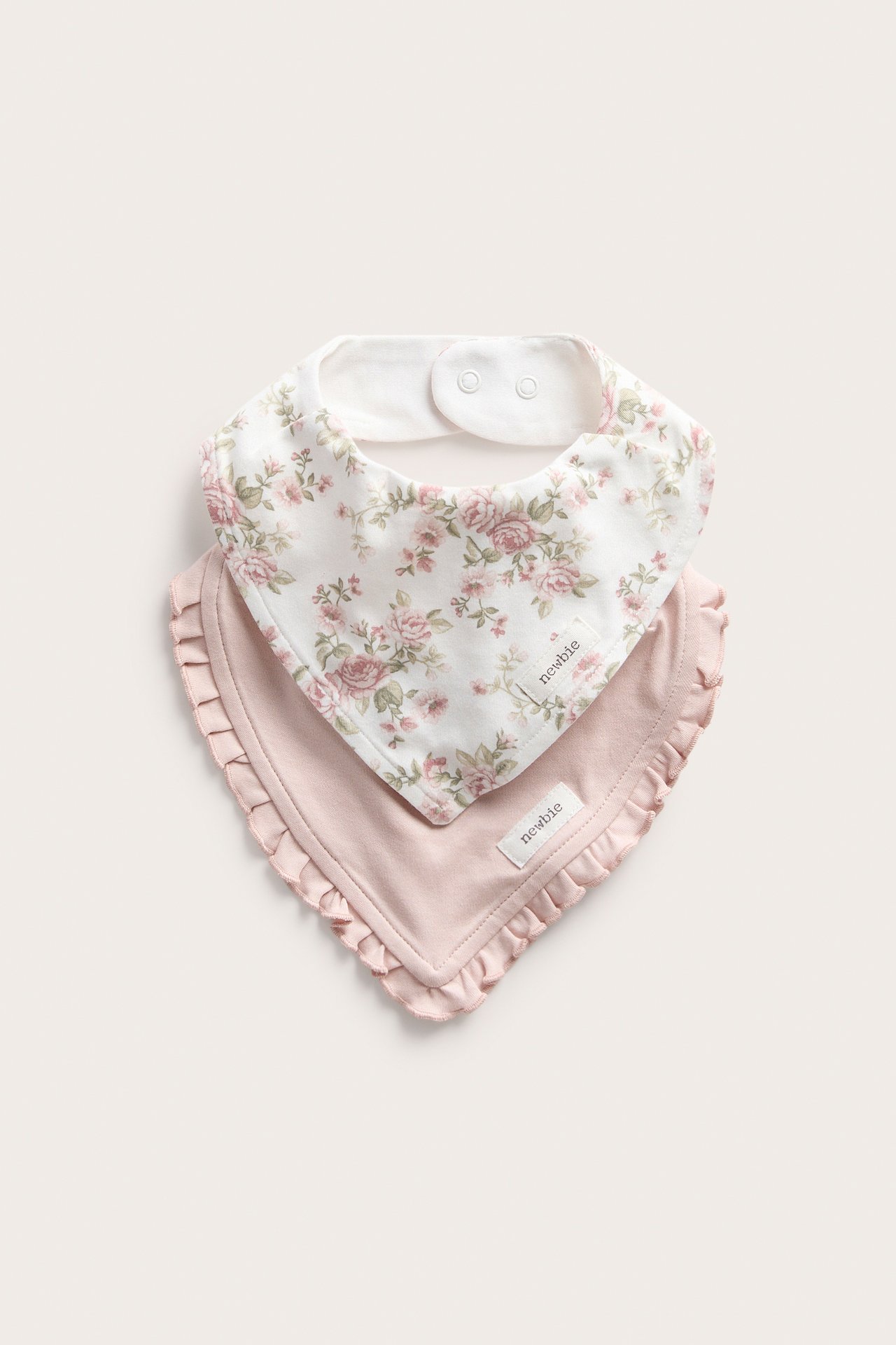 Front view: Two baby bibs. One off-white with pink floral print, one light pink with a ruffled edge.