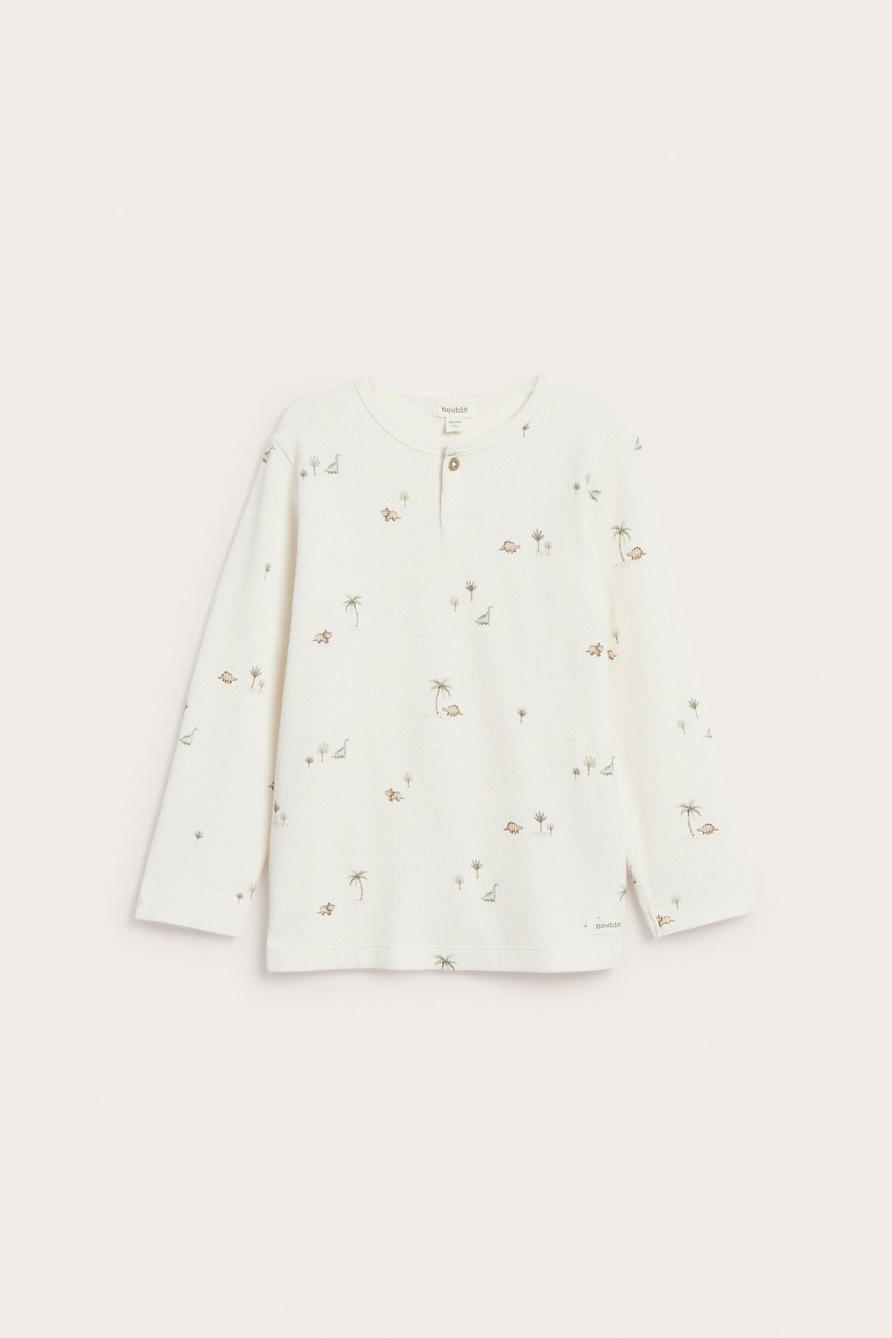 Front view of an off-white kid's waffle knit long-sleeved t-shirt with dinosaur and palm tree pattern and button placket.
