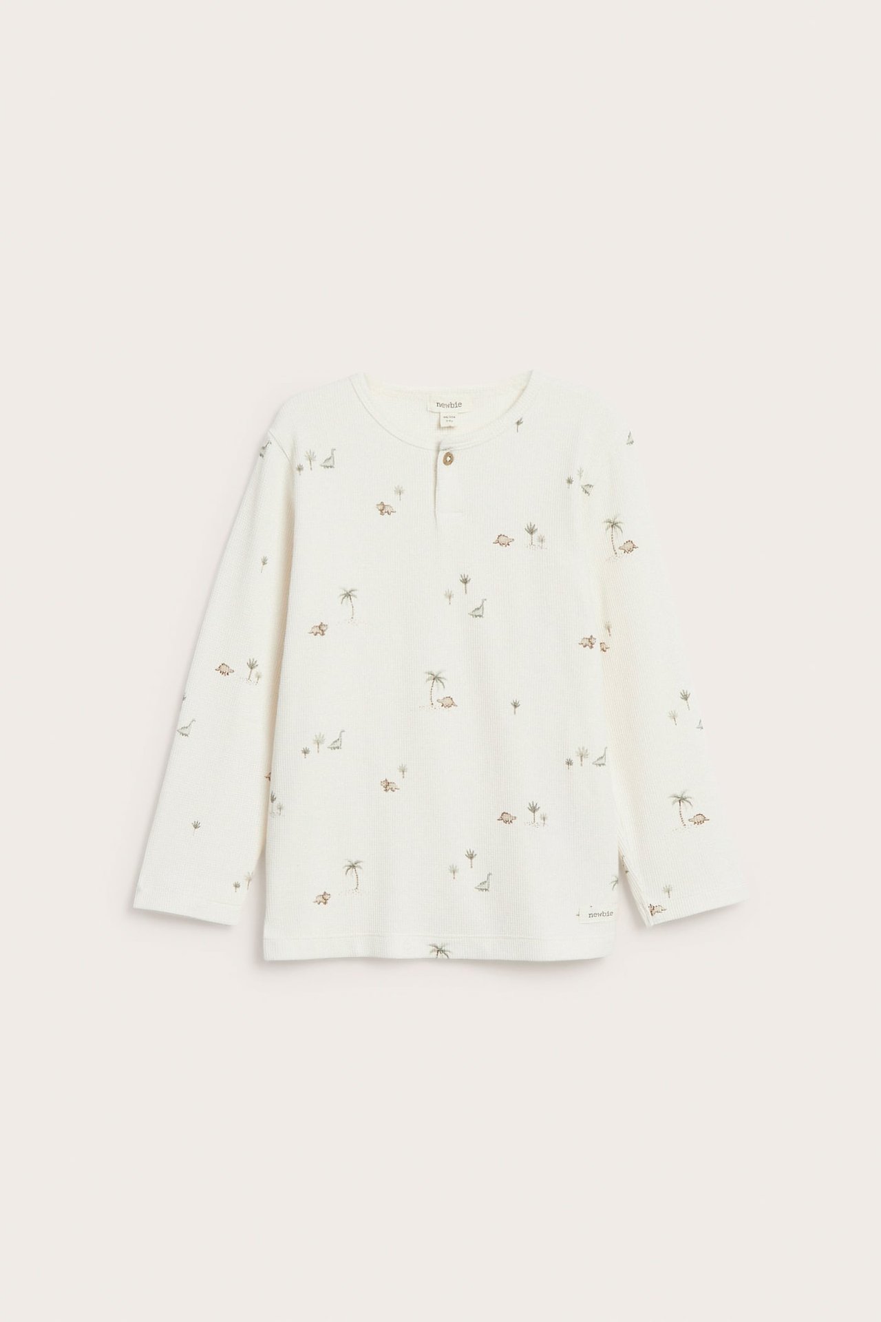 Vorderansicht: ein cremefarbenes Kinder-Langarmshirt aus Waffelstrick mit Dinosaurier- und Palmenmuster, Knopfleiste.