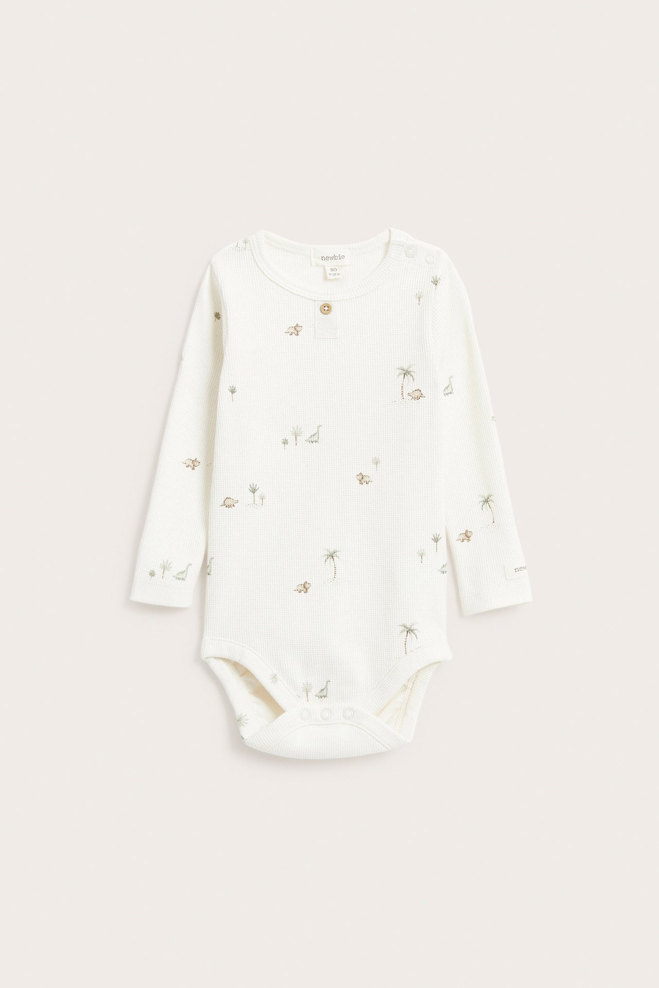 Vorderansicht eines cremefarbenen langärmeligen Waffel-Babybodys mit Dinosaurier- und Palmenmuster.
