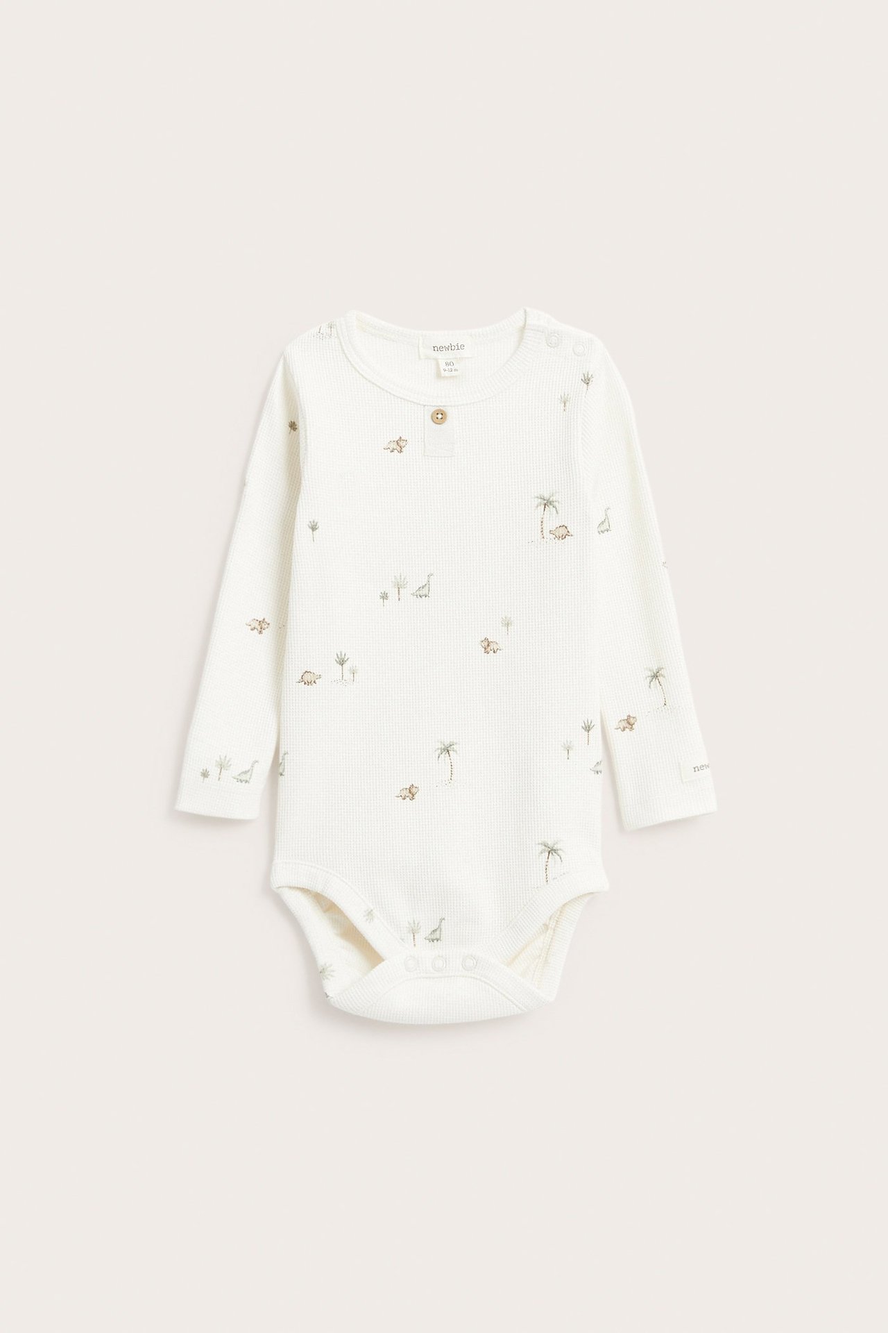 Vorderansicht eines cremefarbenen langärmeligen Waffel-Babybodys mit Dinosaurier- und Palmenmuster.