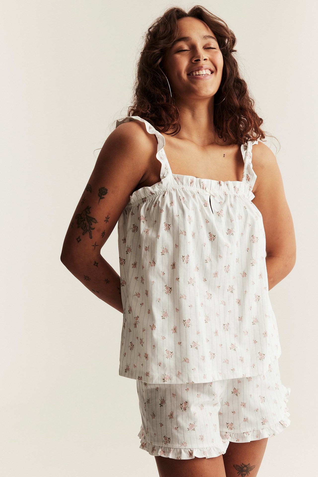 Frontansicht lächelnder Frau in cremefarbenem Baumwoll-Pyjama mit rosa Blumen- und Streifenmuster.