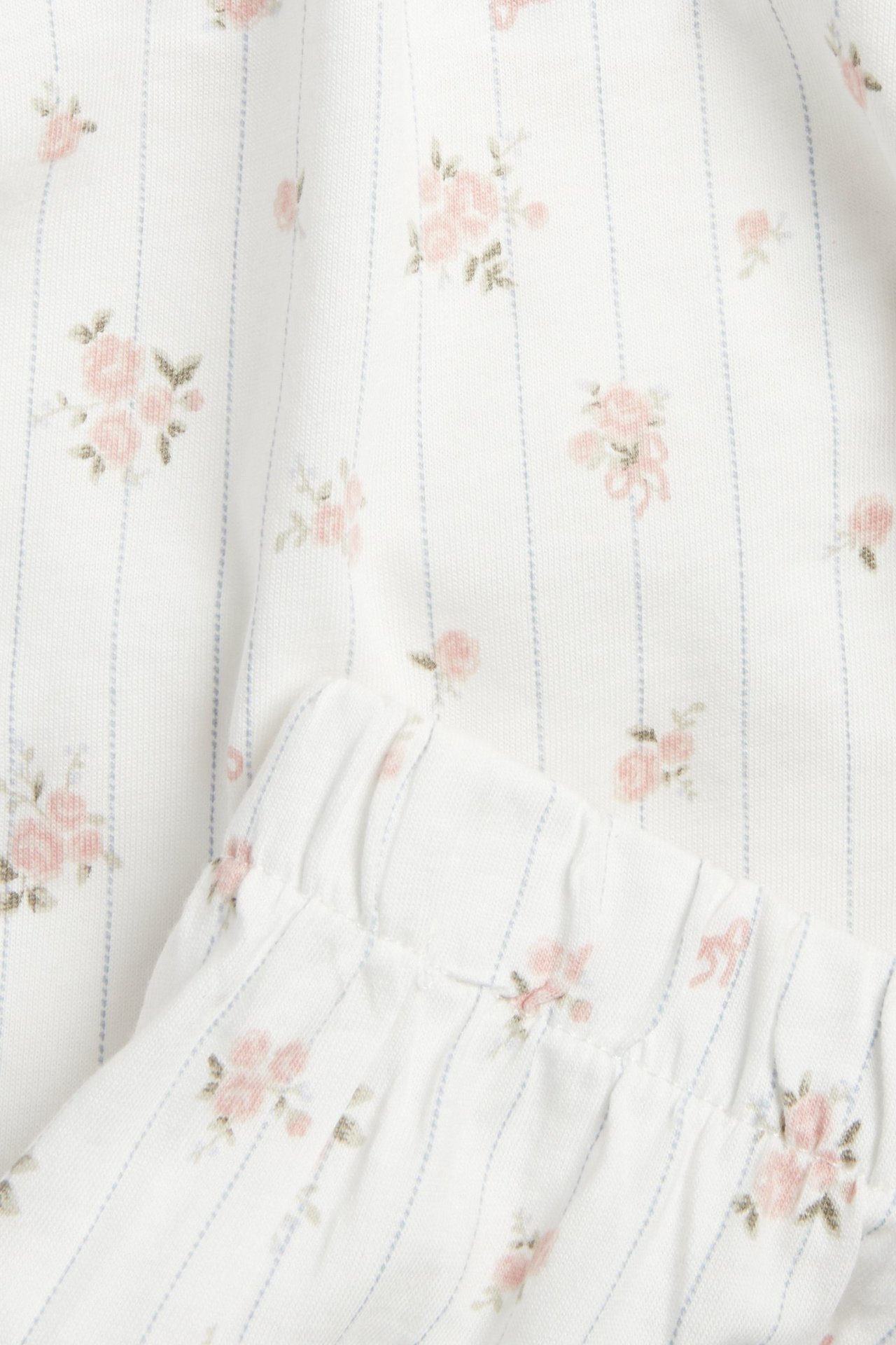 Close-up of off-white cotton pajamas fabric with blue stripes and pink floral print, featuring an elastic waistband.