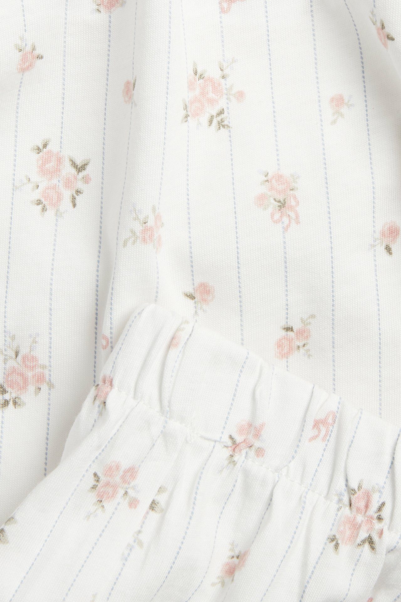 Nahaufnahme von cremefarbenem Baumwollpyjama-Stoff mit blauen Streifen und rosa Blumenmuster, mit Gummizugbund.