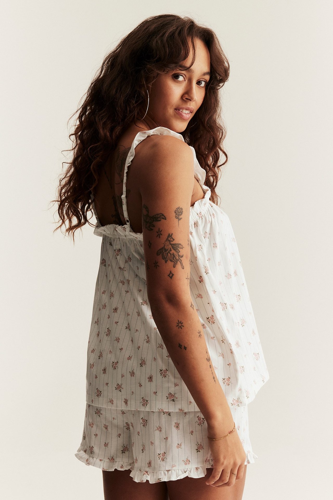 Side view of a woman wearing off-white cotton floral pyjamas with ruffles on top and shorts.