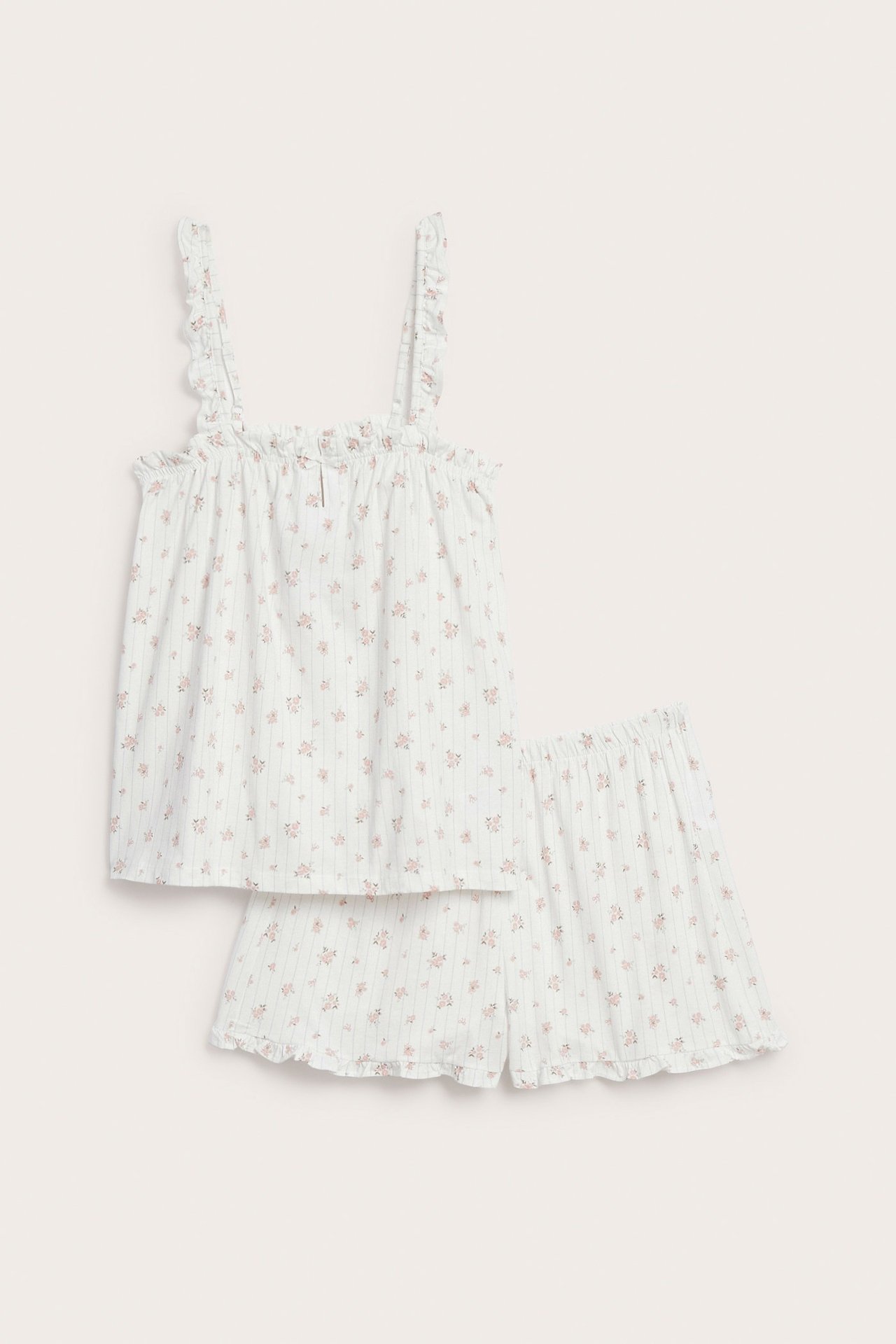 Front view of an off-white cotton woman's pyjamas set with pink floral pattern, ruffled adjustable straps, and elastic shorts.