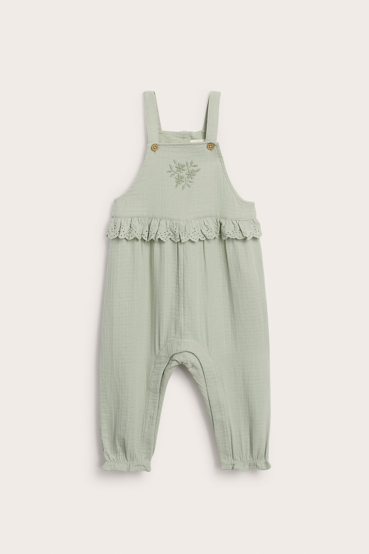 Vorderansicht von hellgrünen Baby-Baumwoll-Latzhosen mit Blumenstickerei und Spitzenrüsche an der Taille.