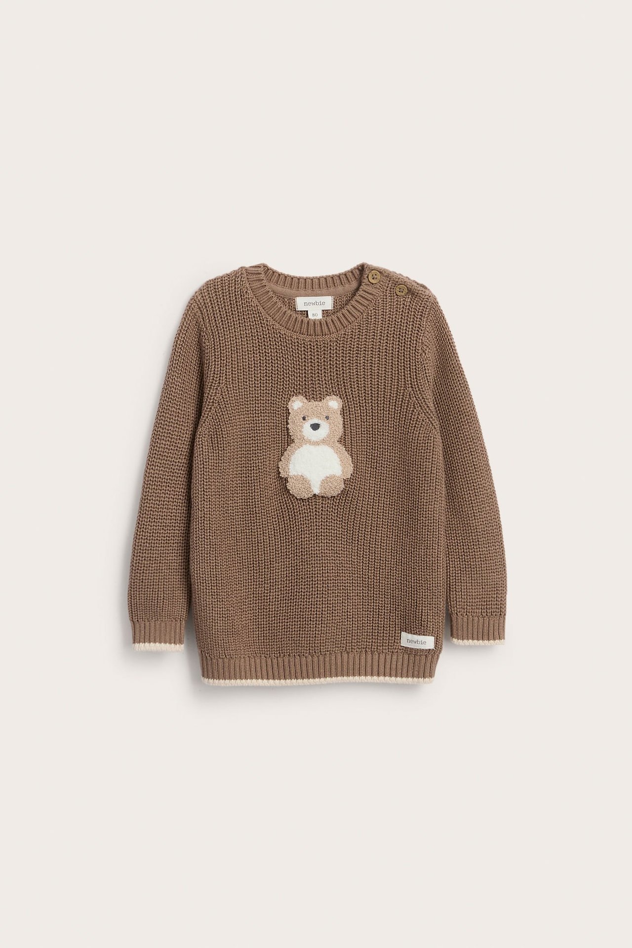 Front view of a brown knitted baby sweater with a teddy bear appliqué and shoulder buttons.