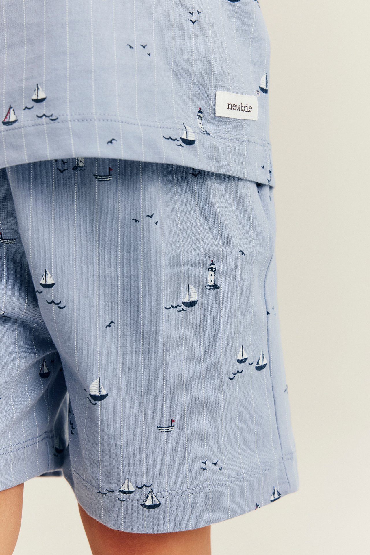 Close-up of a kid's light blue cotton pajama set with white stripes, sailboat, and lighthouse pattern.