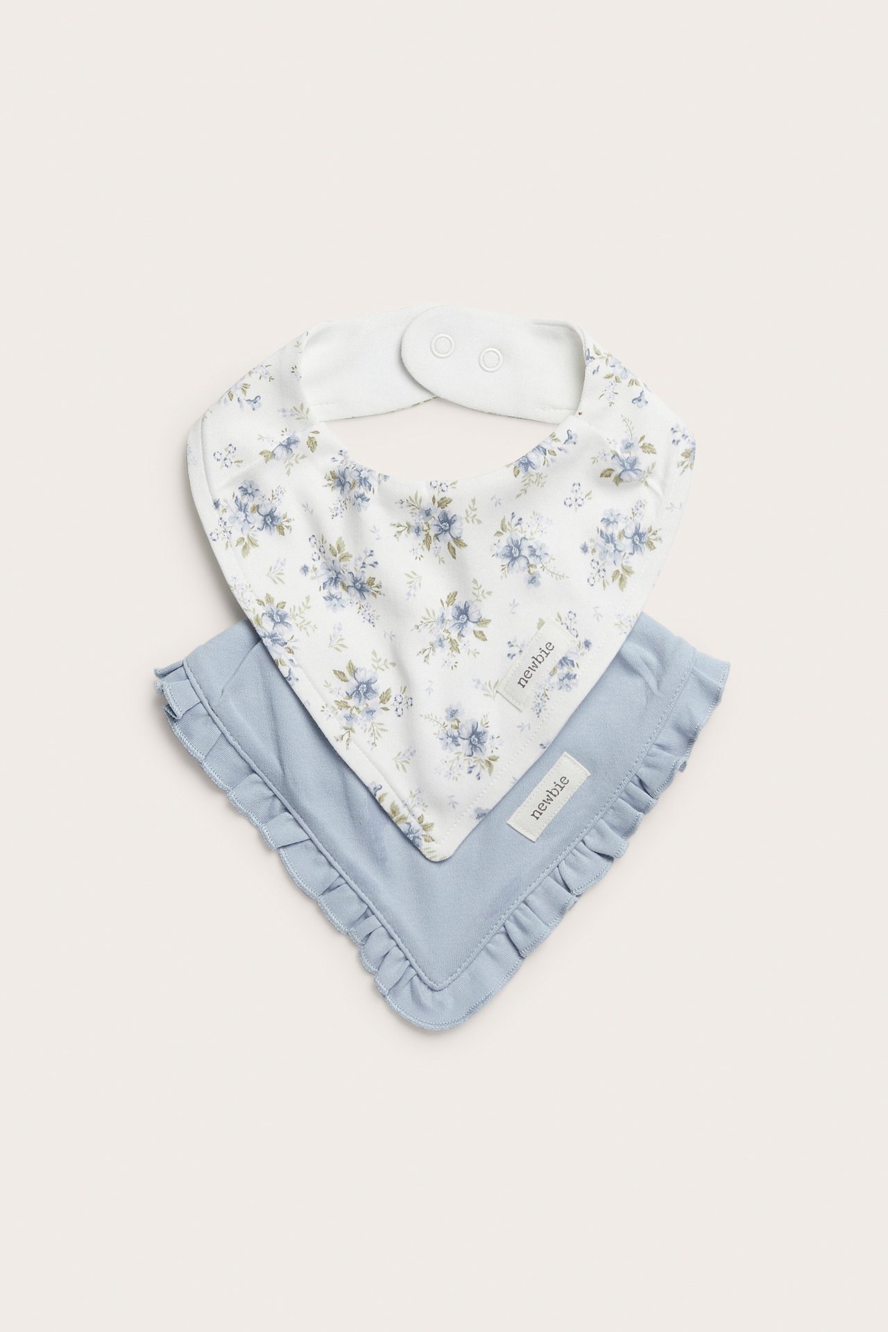 Front view of two cotton baby bibs: an offwhite floral and a light blue with ruffle trim.