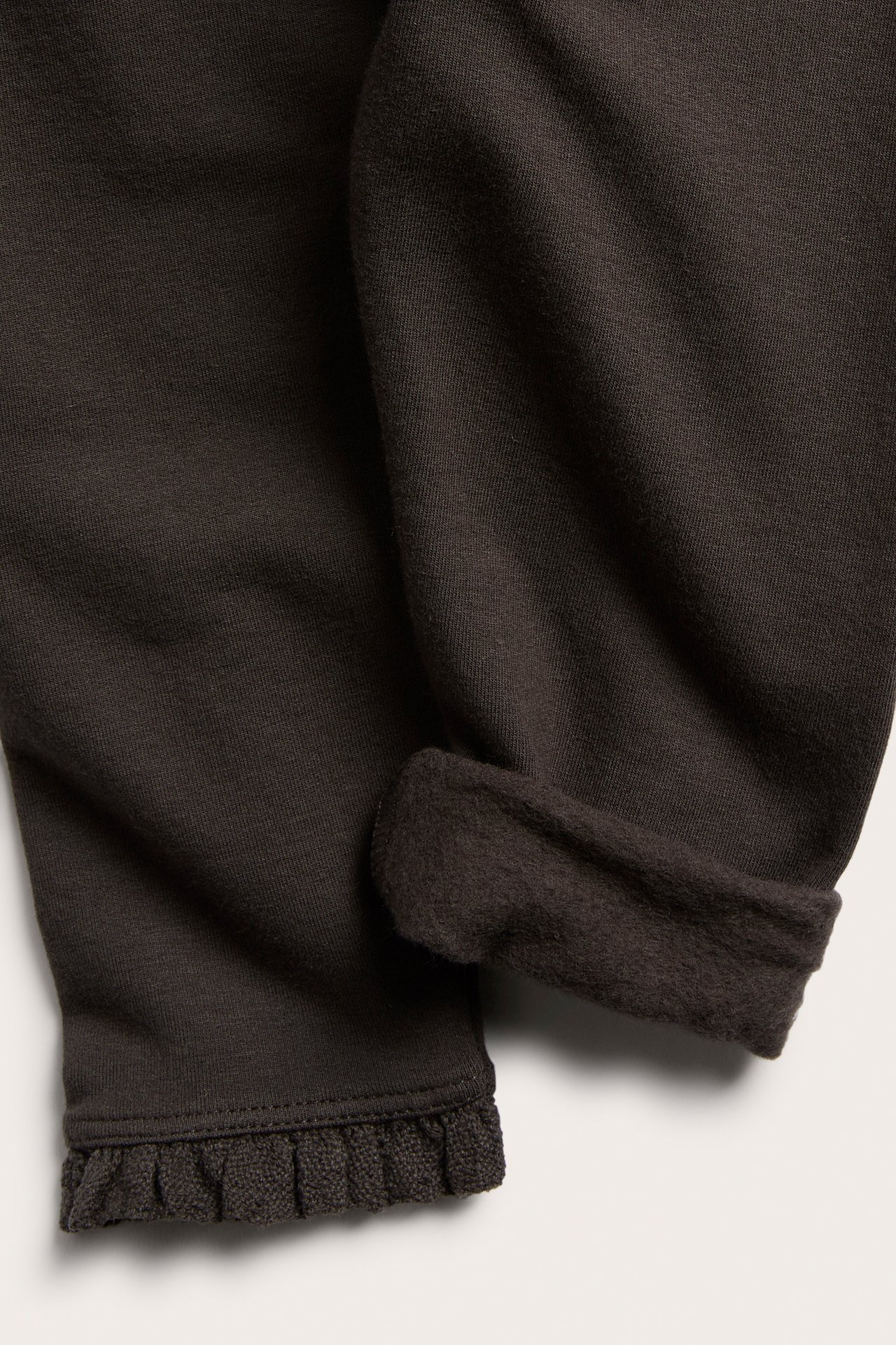 Nahaufnahme eines dunkelbraunen Strickkleidungsstücks mit gekrempeltem Rand, der weiches Futter zeigt, und einem Rüschensaum.