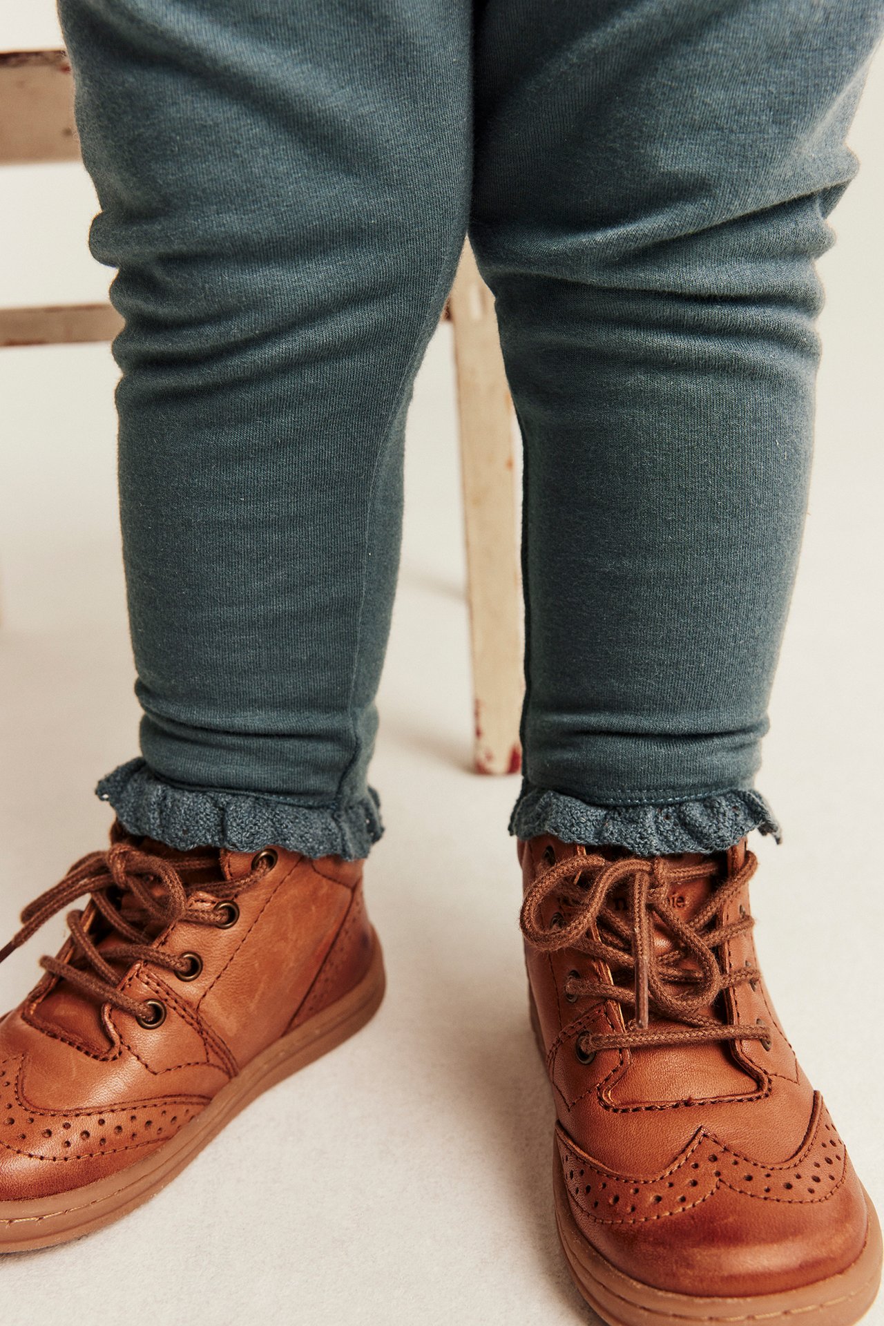 Nahaufnahme, Vorderansicht, von Kinder-Leggings aus dunkelgrünem Jersey mit Rüschensaum über braunen Schnürstiefeln.
