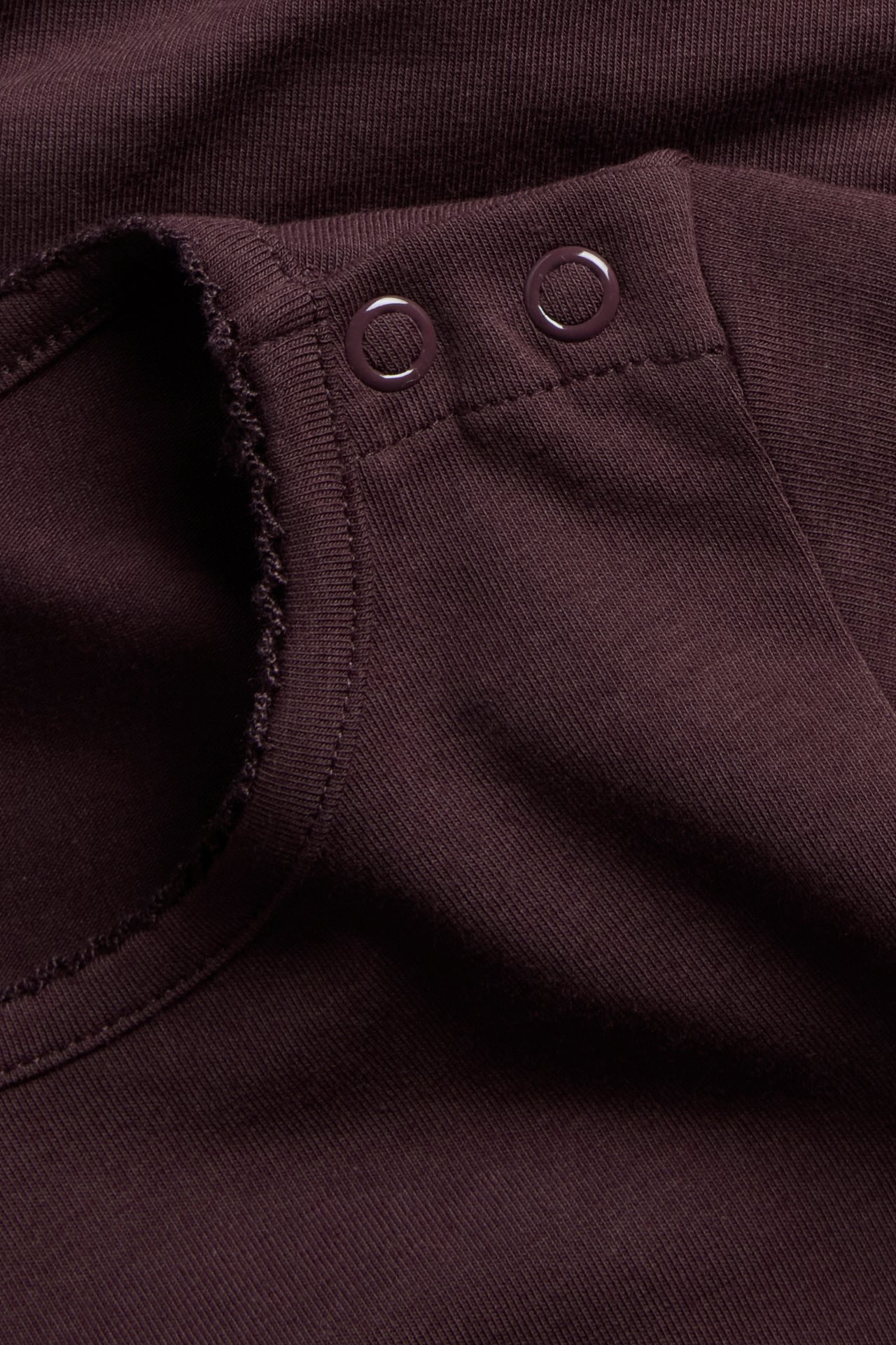 Close-up of a dark red ribbed knit garment with two round snap fasteners.