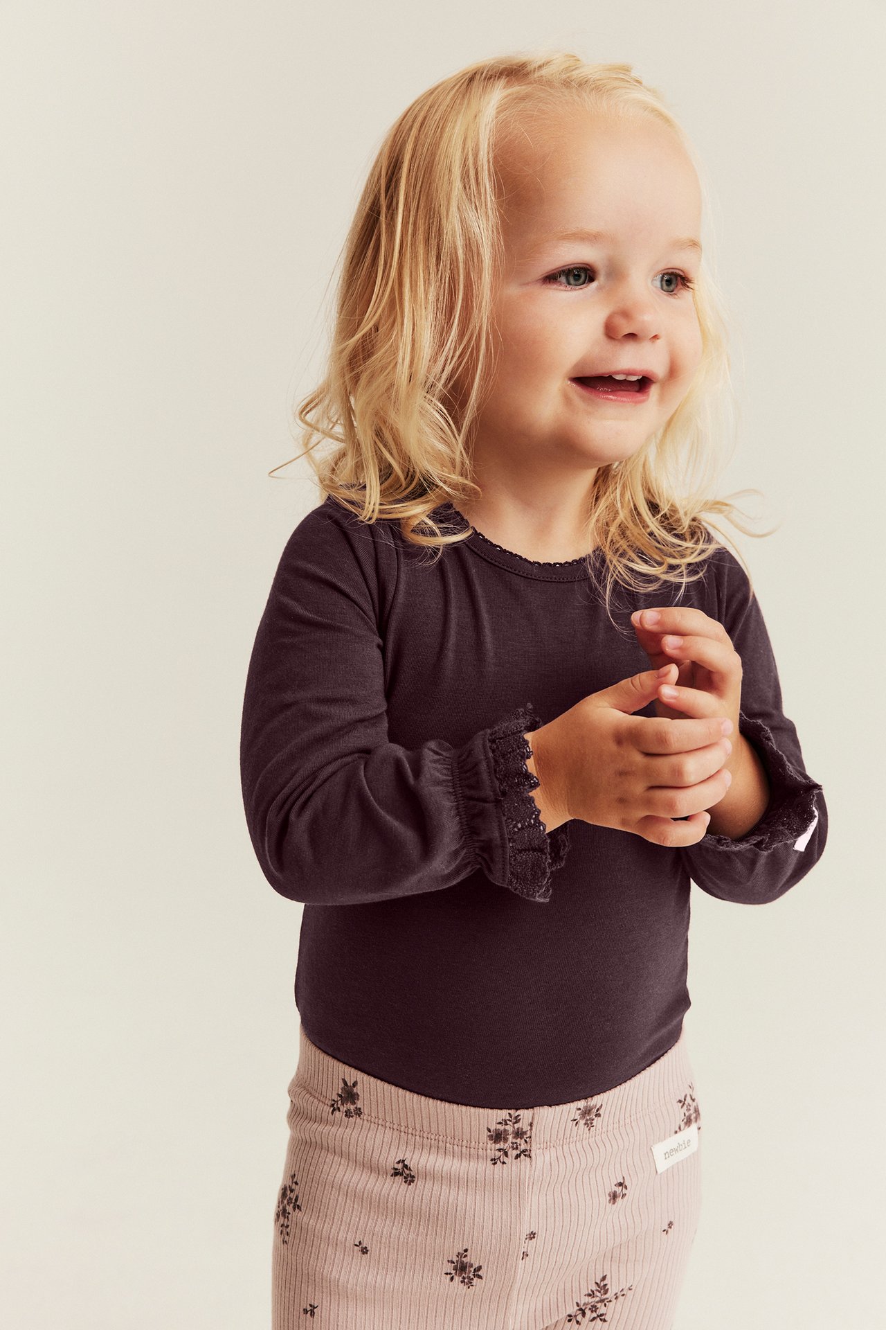 Dunkelviolettes Langarmshirt mit Spitzenmanschetten und rosa geblümten Rippenleggings an Kind.