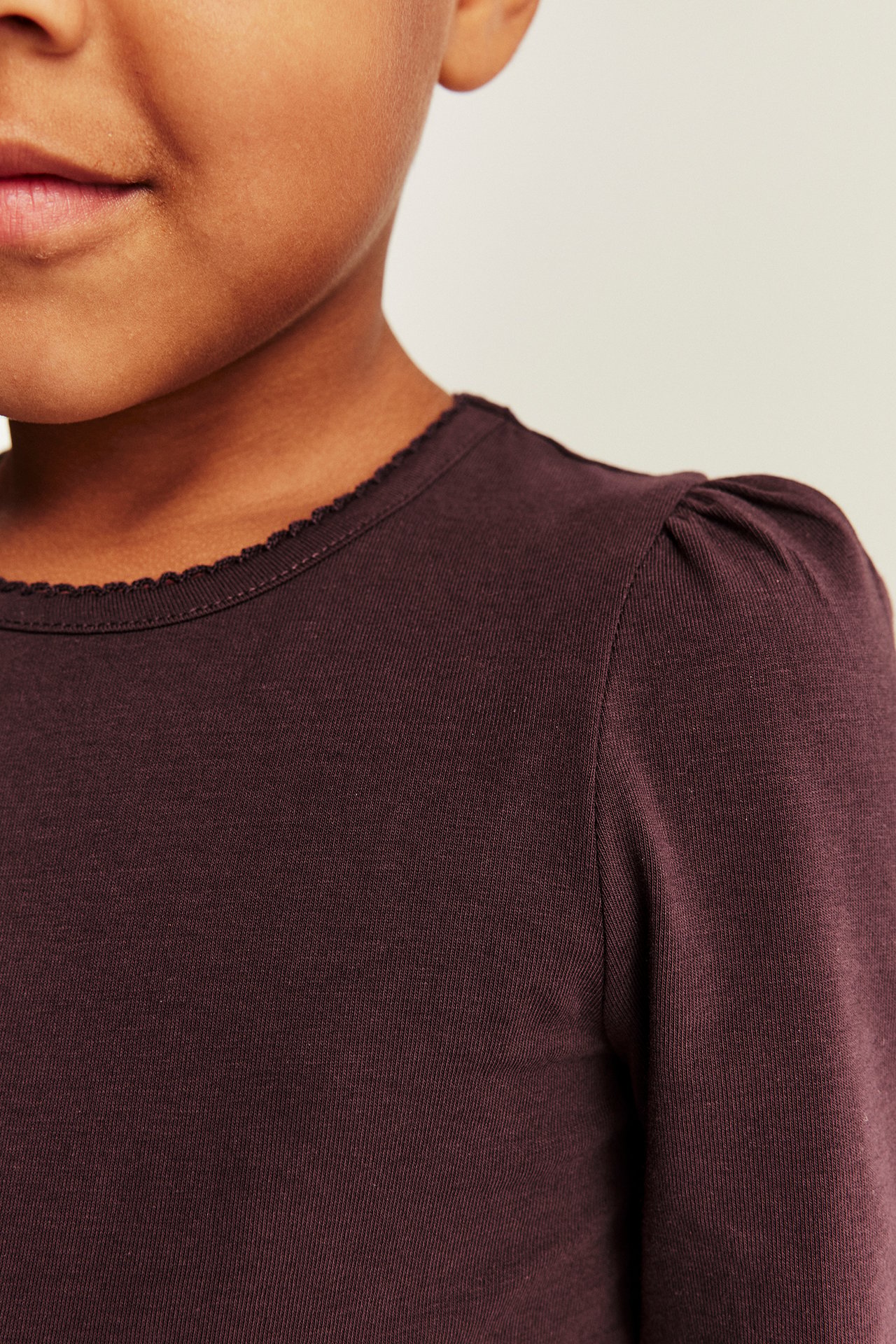 Close-up of a kid's dark purple long-sleeved top with a scalloped neckline and puff sleeves.