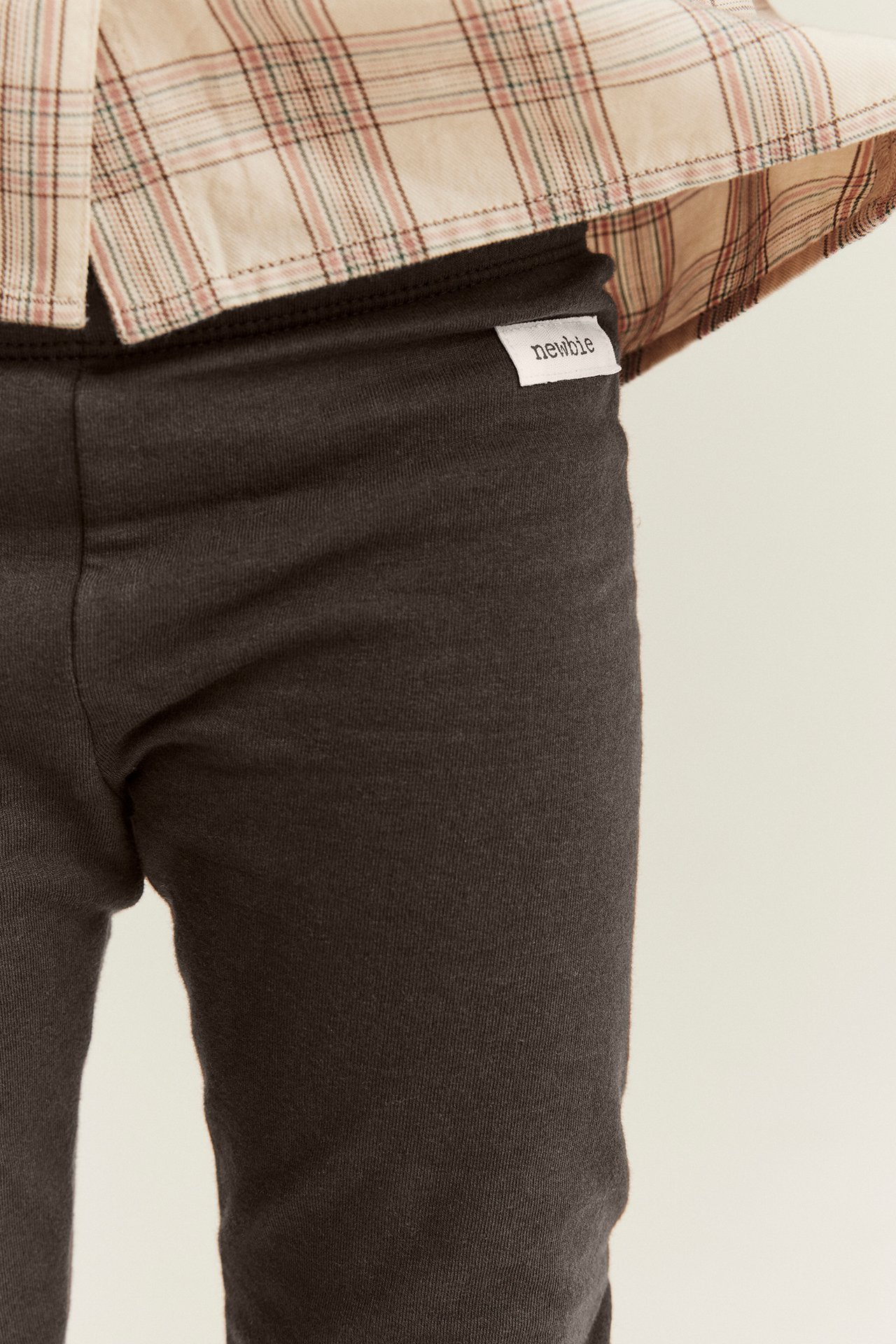 Close-up of kid in dark grey jersey leggings with a white tag and a light plaid shirt.