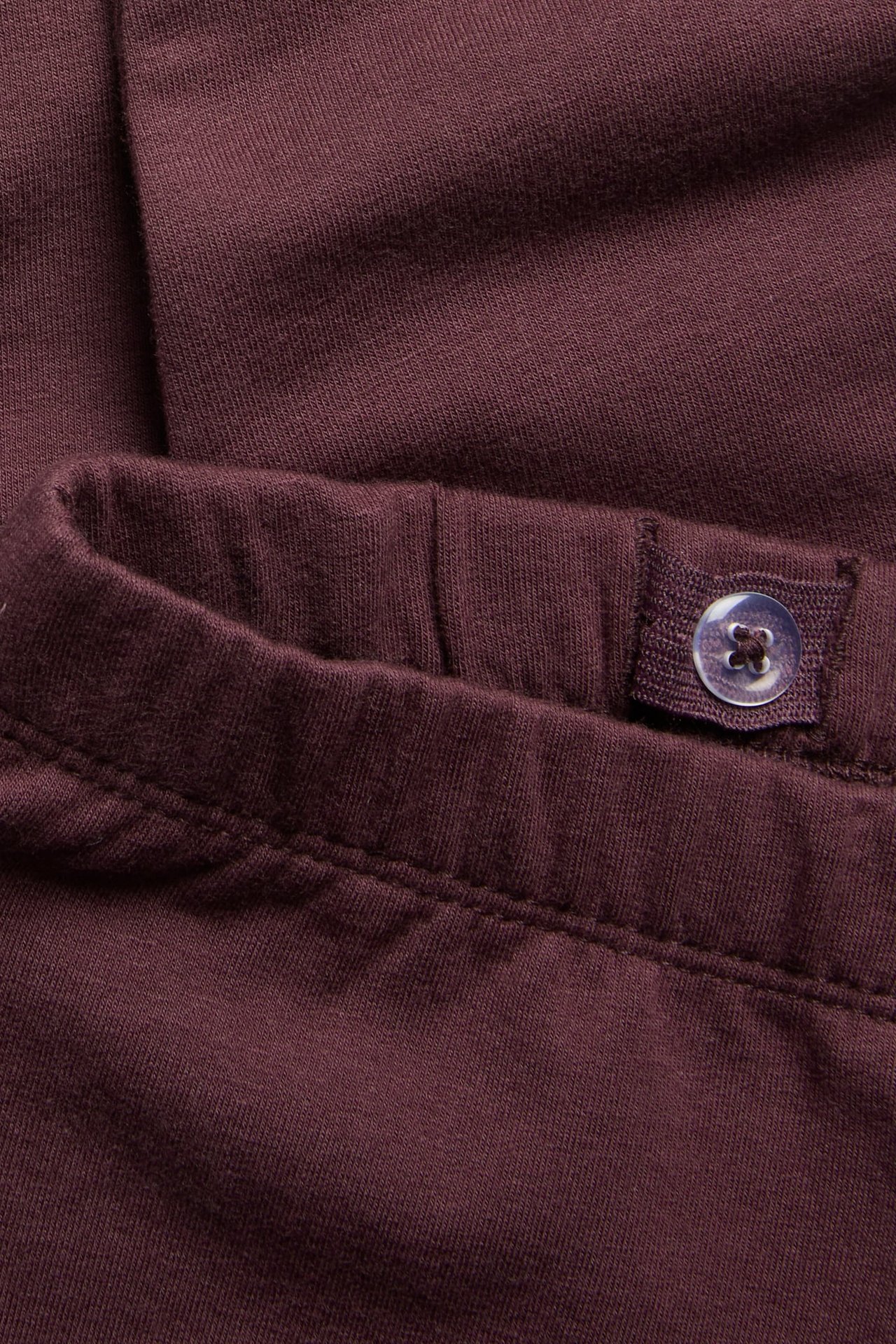 Nahaufnahme einer dunkelroten Jerseyhose mit verstellbarem Gummibund und Knopf.
