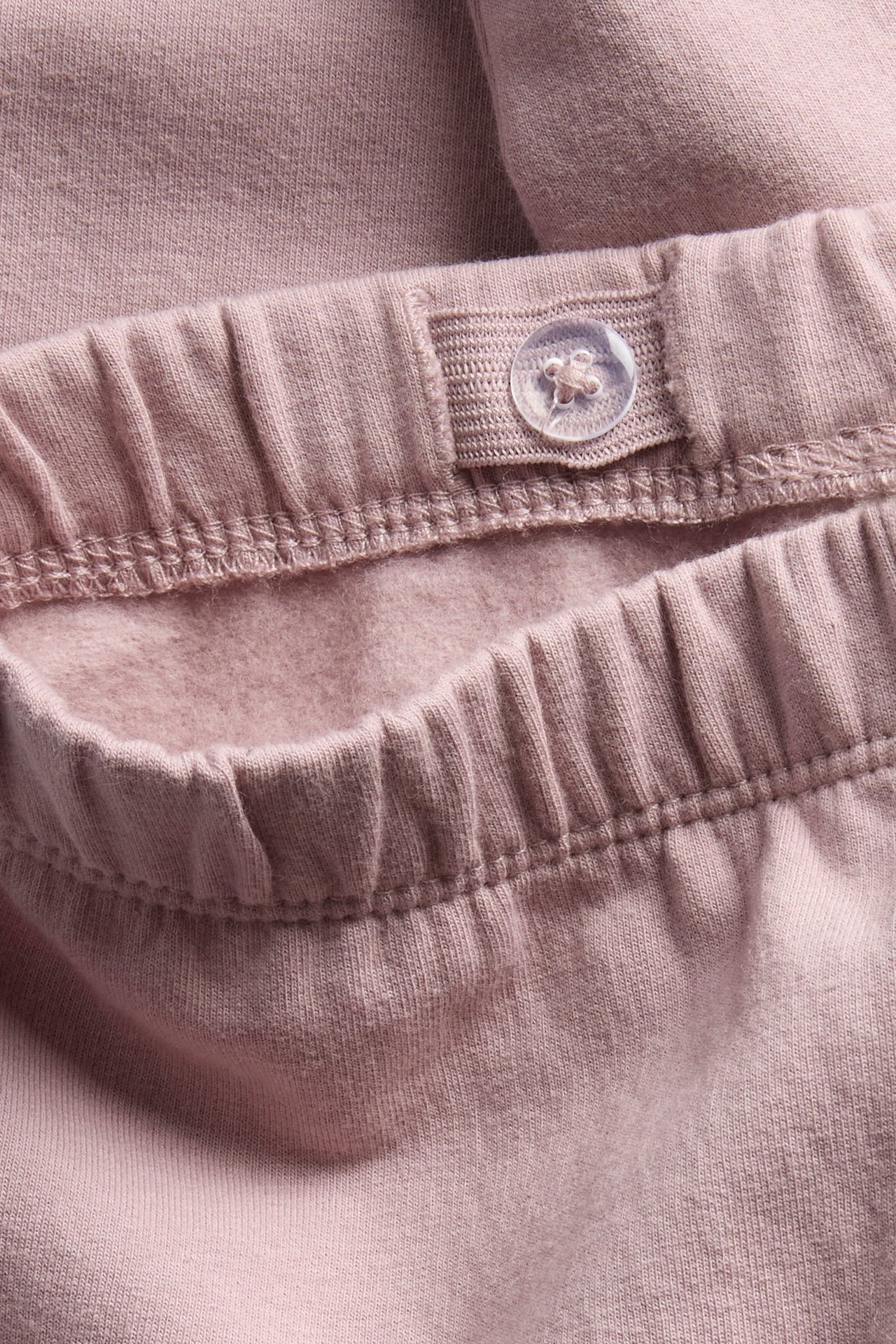 Nahaufnahme des staubrosa Jogginghosen-Bundes mit verstellbarem Gummiband und klarem Knopf.