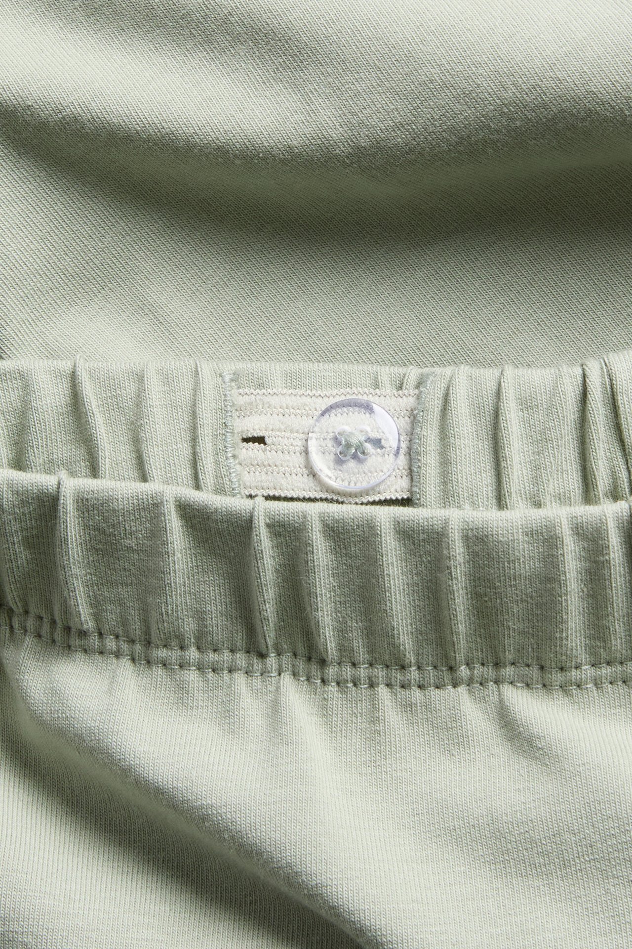 Close-up of green cotton leggings showing an adjustable elastic waistband with a clear button.