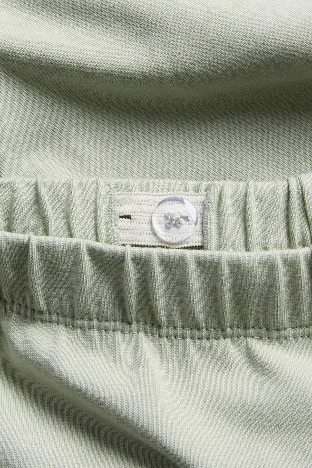 Nahaufnahme von grünen Baumwoll-Leggings mit verstellbarem Gummibund und transparentem Knopf.