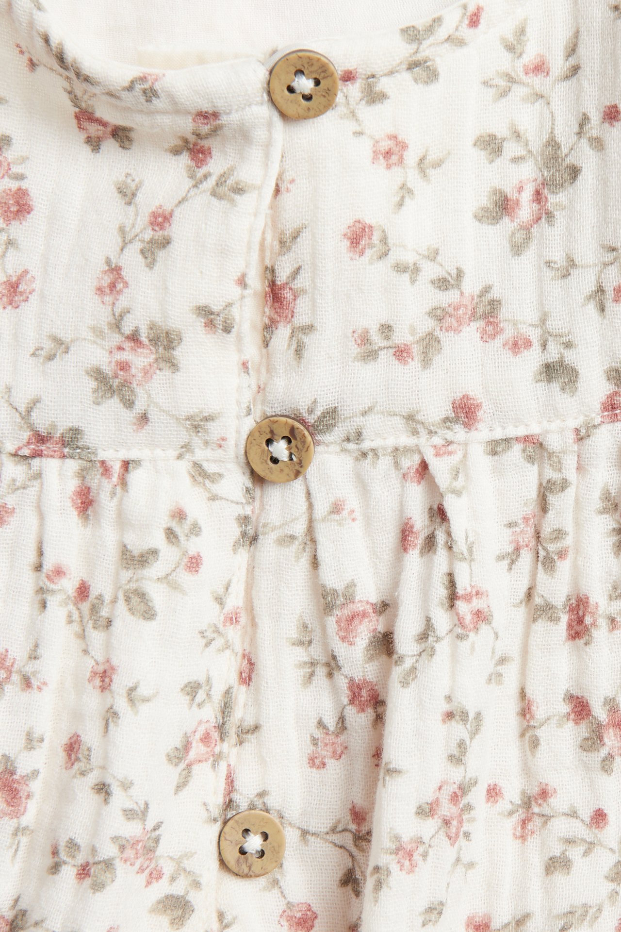 Close-up of off-white muslin blouse with small floral pattern and wooden buttons.