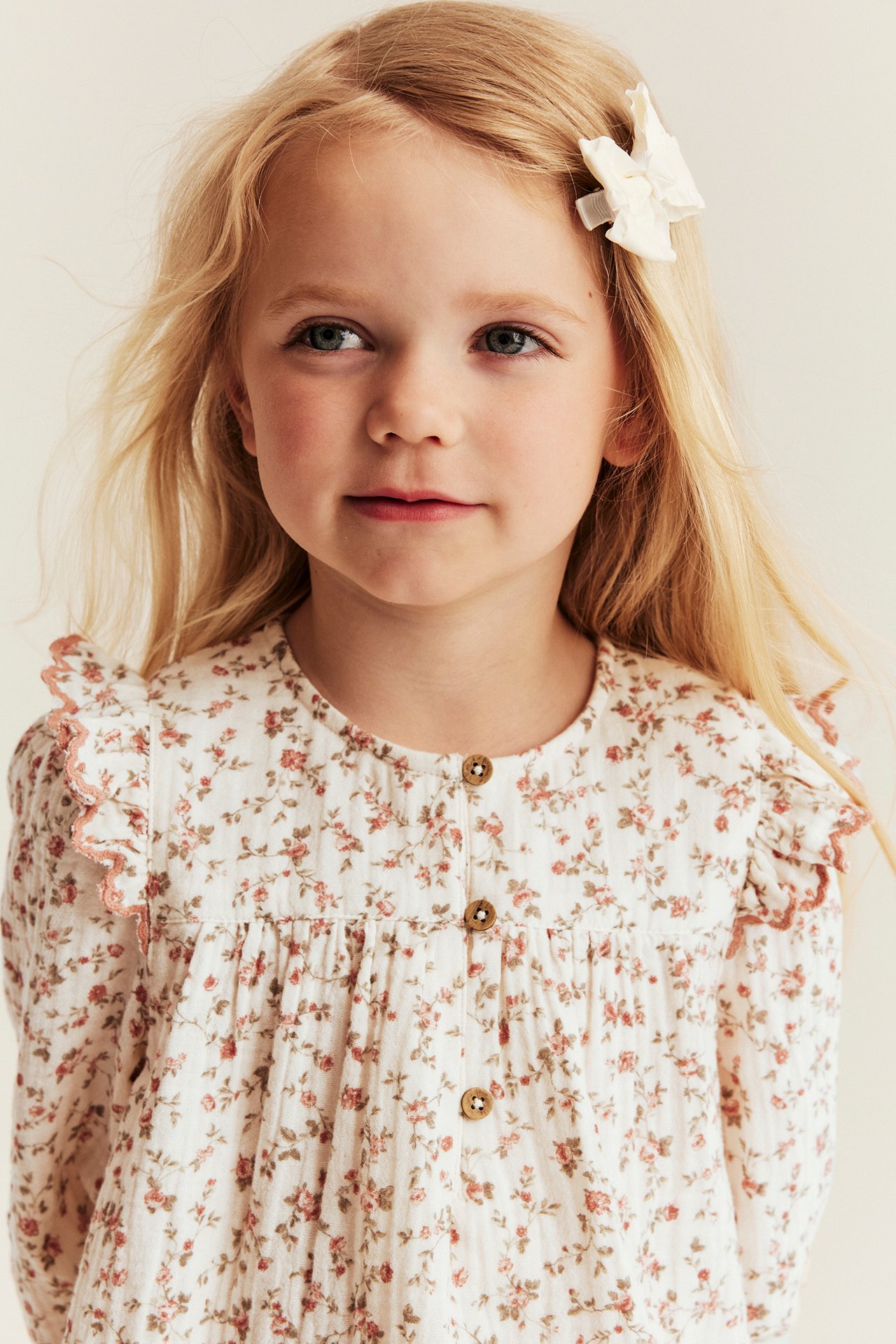 Front view of a kid wearing an off-white floral muslin blouse with shoulder ruffles and front buttons.