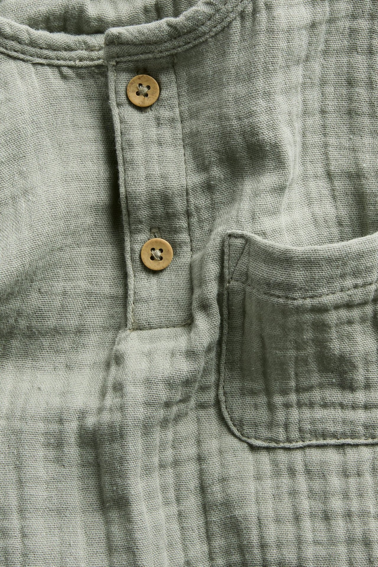 Close-up of a dark green crinkled cotton muslin long-sleeved top with a button placket and chest pocket.