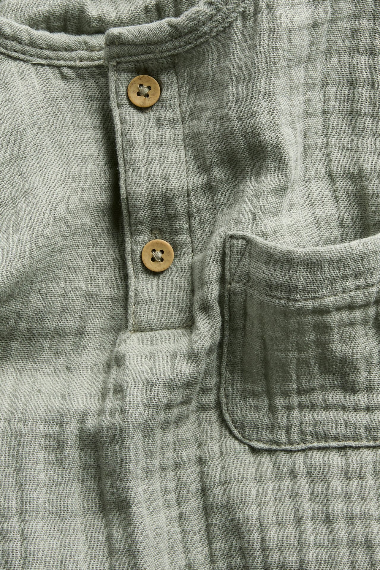 Nahaufnahme eines dunkelgrünen, gekräuselten Baumwoll-Musselin Langarmtops mit Knopfleiste und Brusttasche.