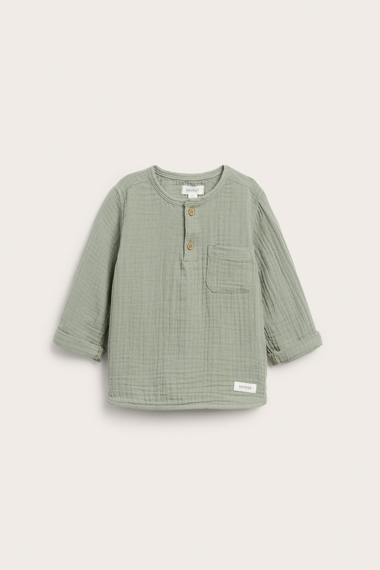 Front view: Kid's long-sleeved sage green muslin top with button placket, patch pocket, and rolled cuffs.