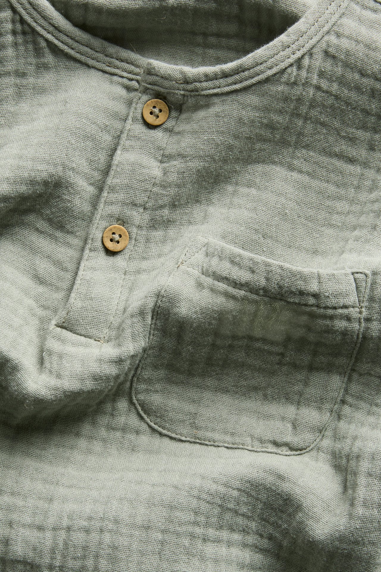 Vorderansicht, Nahaufnahme eines hellgrünen, langärmeligen Baumwoll-Musselin-Oberteils mit Knopfleiste und Brusttasche.