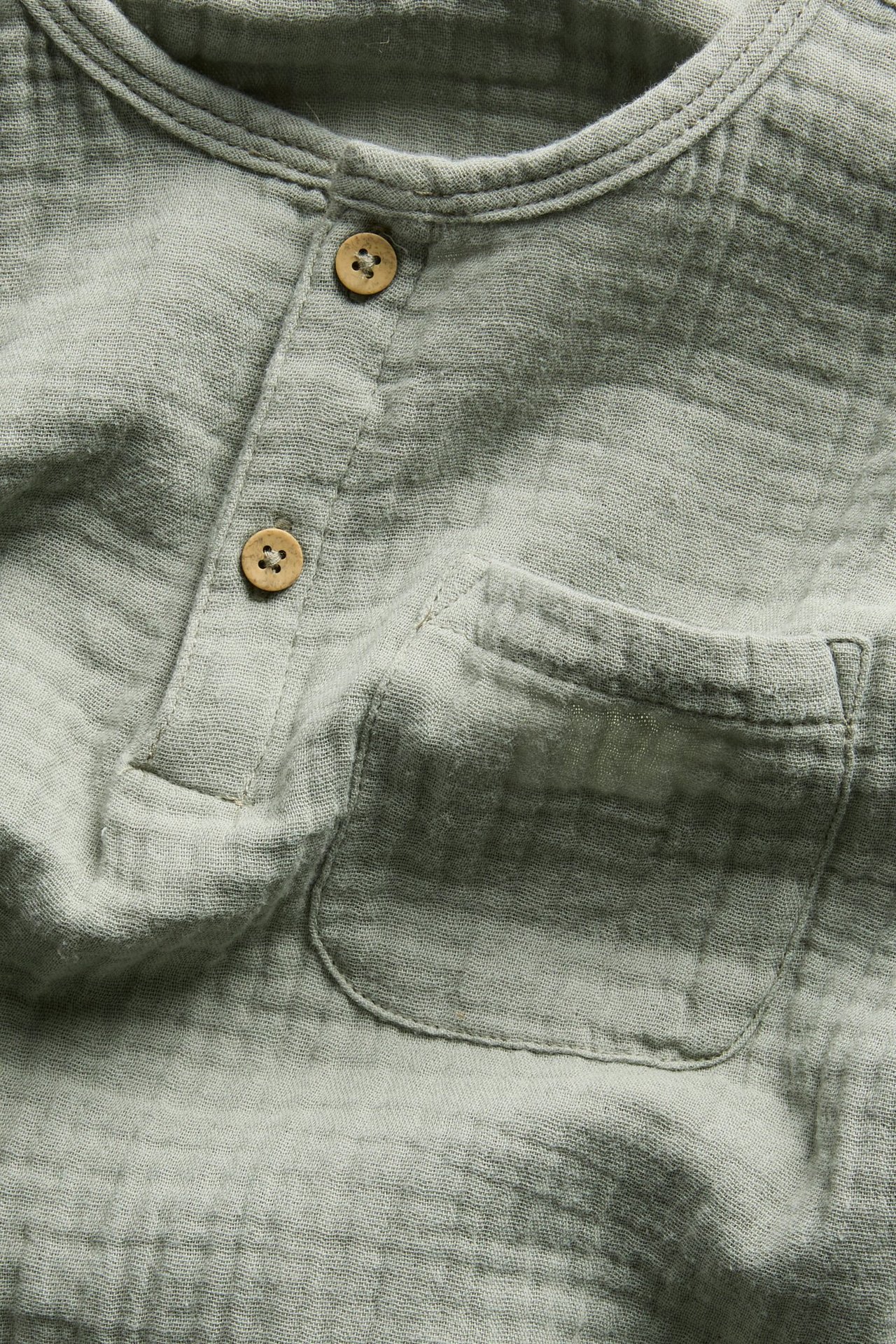 Vorderansicht, Nahaufnahme eines hellgrünen, langärmeligen Baumwoll-Musselin-Oberteils mit Knopfleiste und Brusttasche.