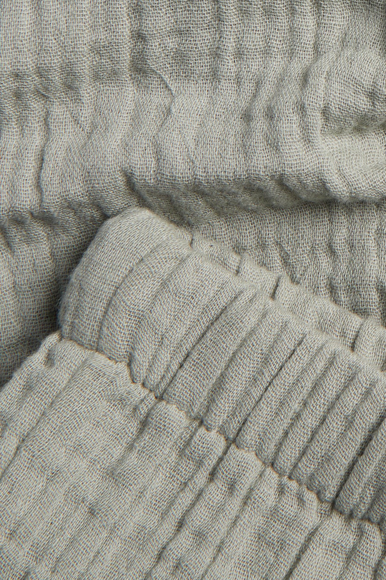 Close-up of light green woven cotton muslin trousers with an elasticated detail.