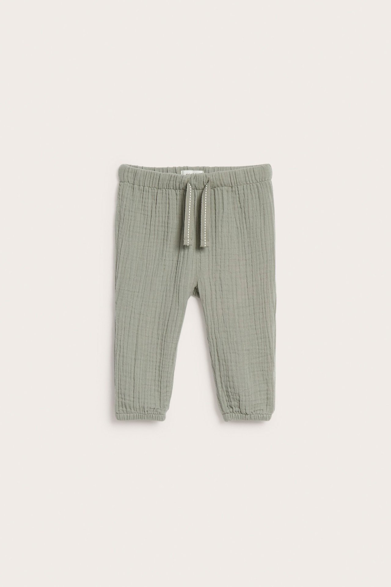 Front view of dark green kid's muslin pants with elastic waist, drawstring, and gathered leg openings.